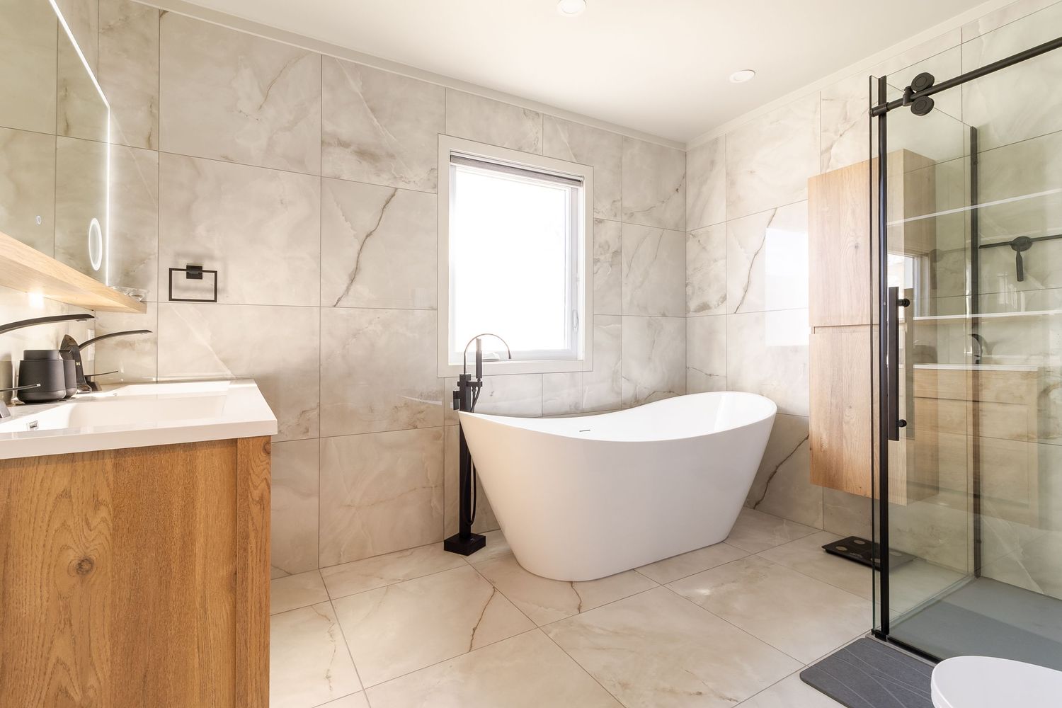 Luxurious bathroom featuring a freestanding tub, marble tile walls, and wooden vanity with modern fixtures.