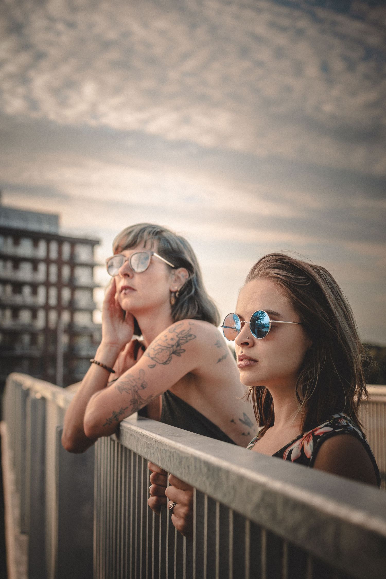 Friends relaxing on a pier railing at sunset wearing sunglasses.