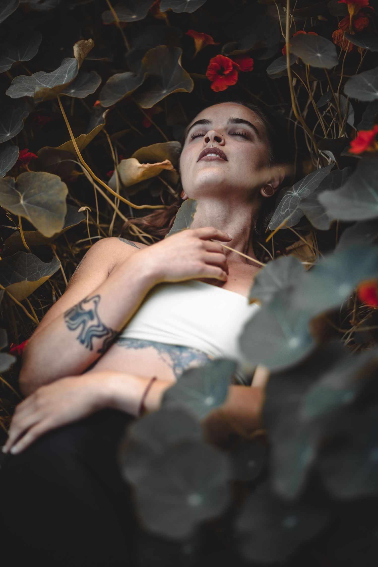 Artistic portrait among red flowers and leaves with dramatic lighting.