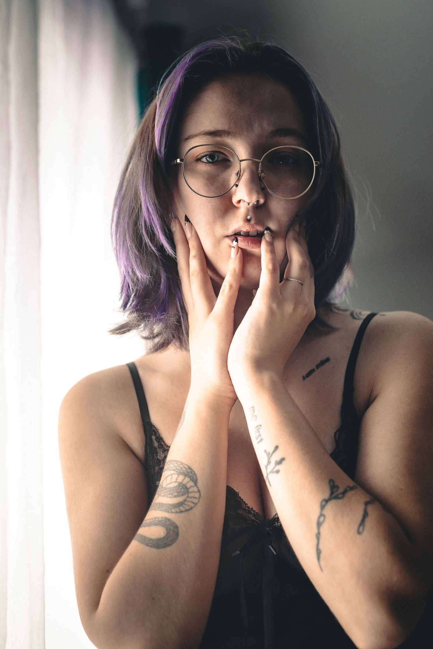 A series of moody portraits showing someone with purple hair and tattoos covering their face with their hands.