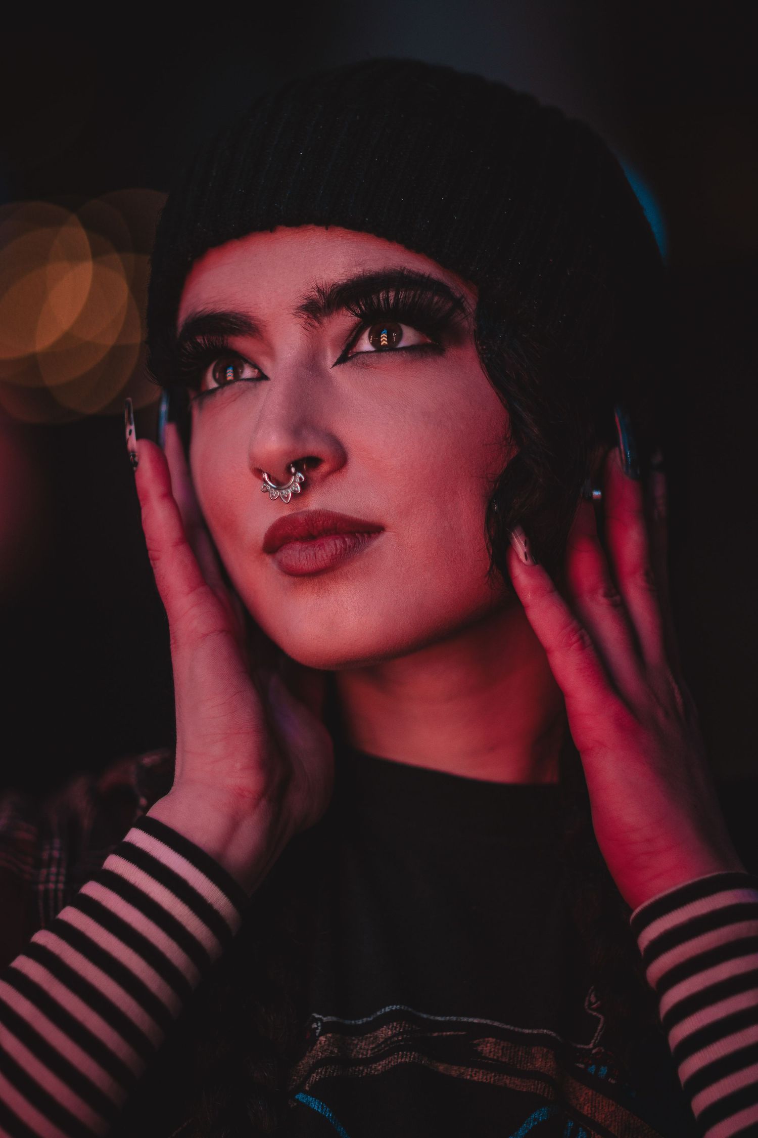 Dark portrait with red lighting showing striped sleeves and dramatic makeup.