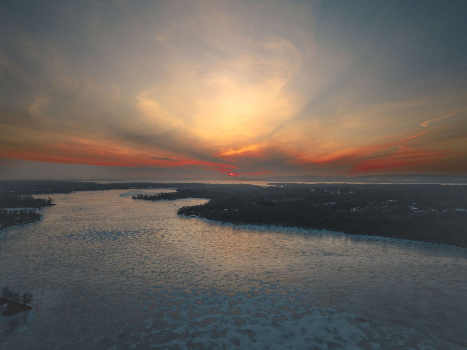 Panoramic sunset over water landscape with dramatic orange sky and reflections.
