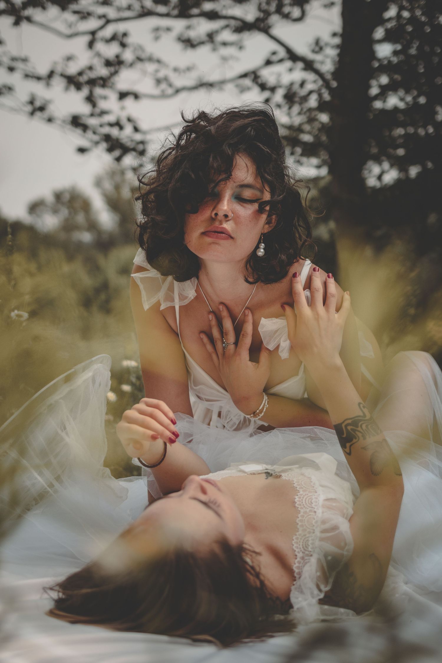 Dreamy outdoor portrait in white dresses with soft bokeh effect through trees.
