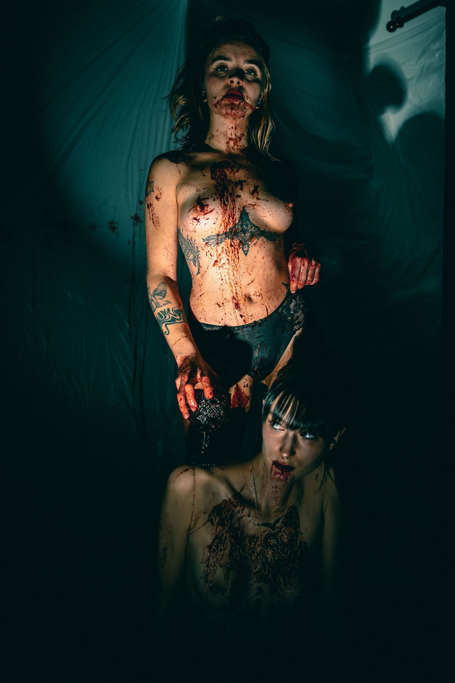 Dark horror scene with blood-covered figures in moody lighting and teal color tones.