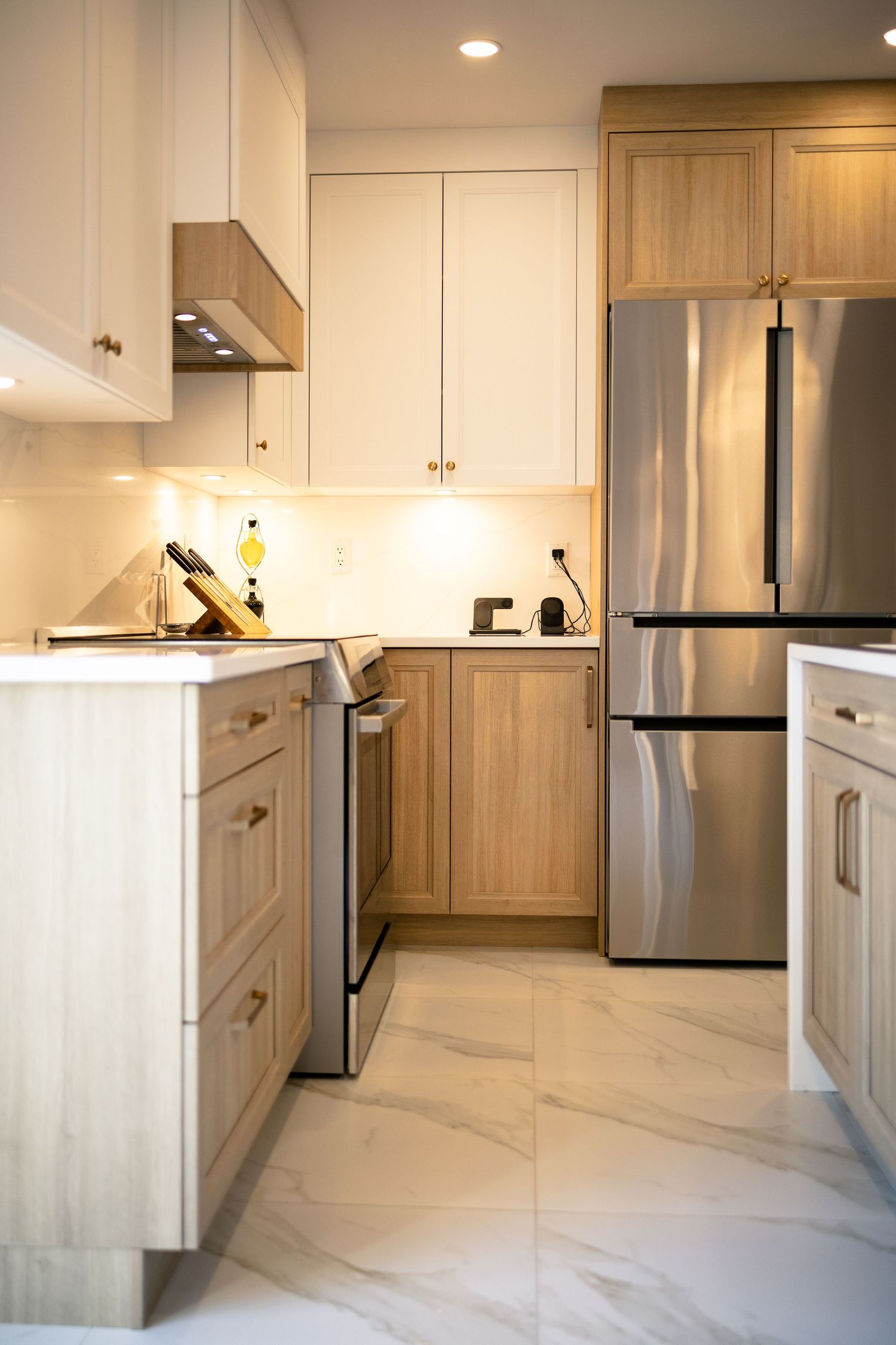 Modern kitchen with light wood cabinets, stainless steel appliances, and marble-look flooring in an open concept layout.