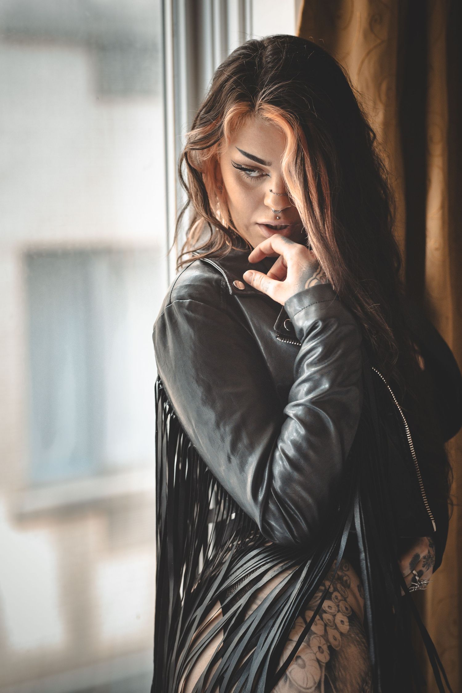 Dramatic indoor portrait with figure in black leather jacket near window.