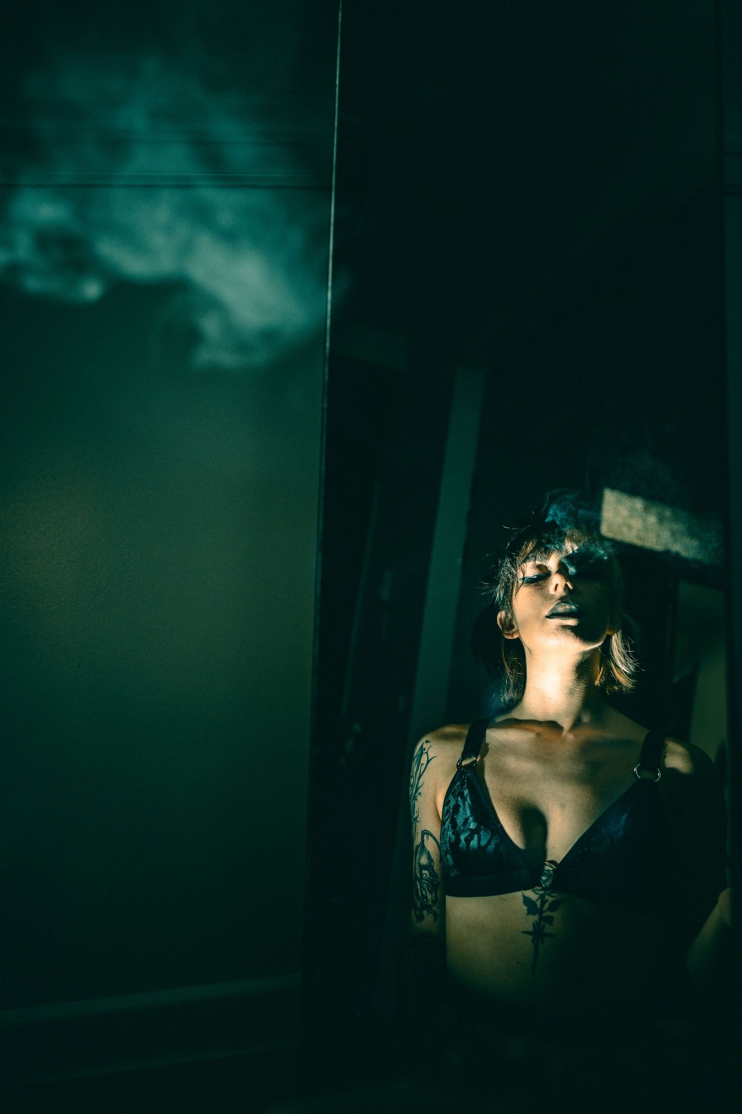 Moody green-tinted portrait through glass with dramatic shadows and lingerie.