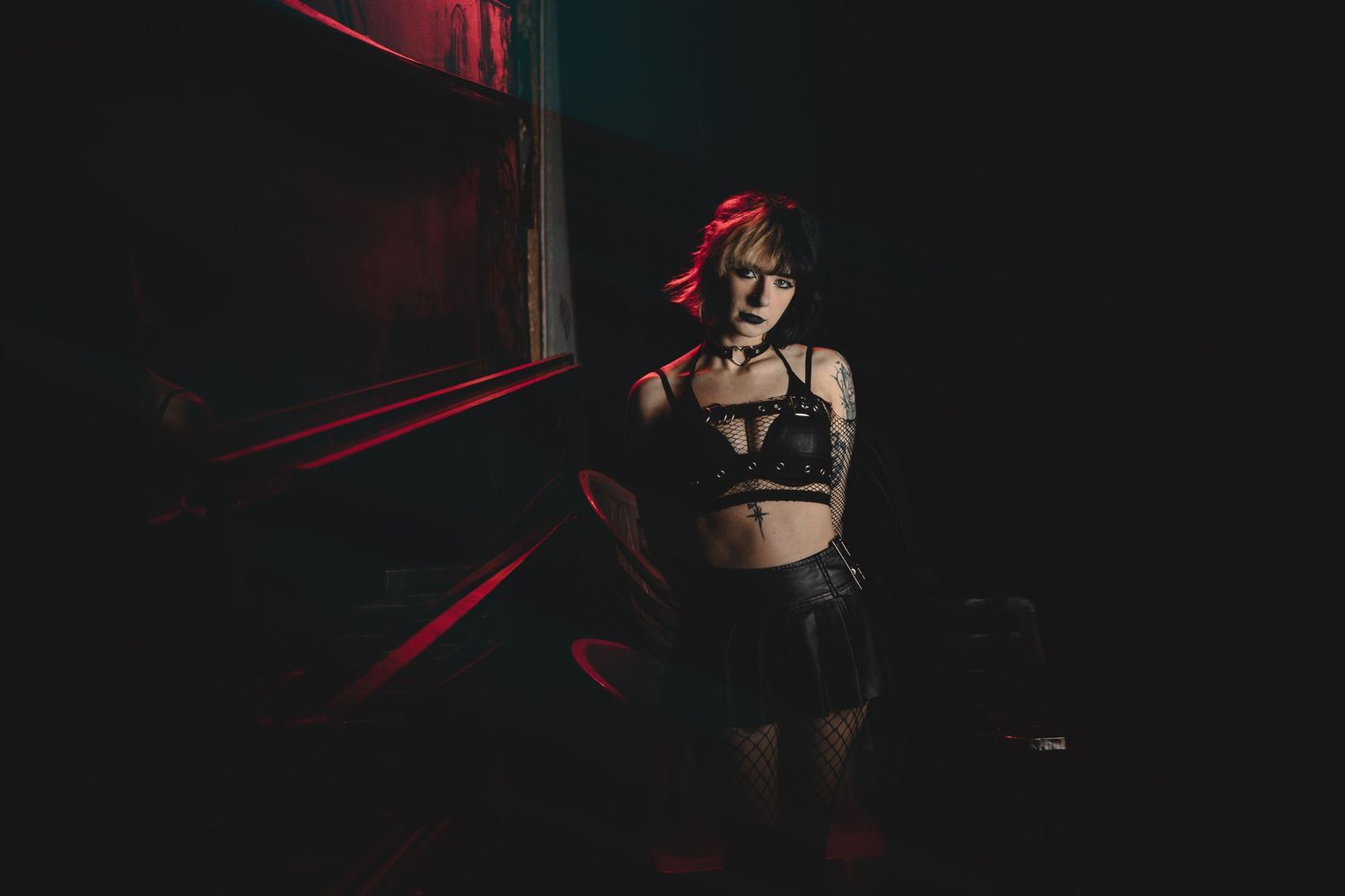 A dark and moody portrait photograph with red lighting accents against a black background.