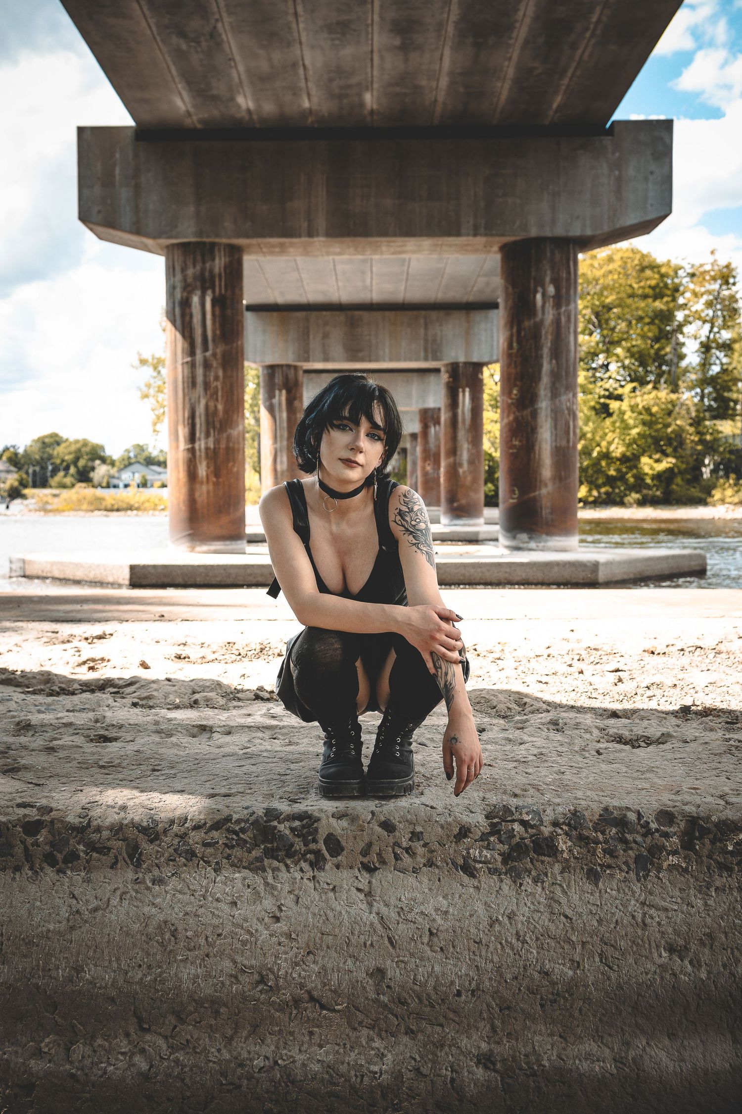 Moody photoshoot under a concrete bridge structure with industrial urban backdrop.