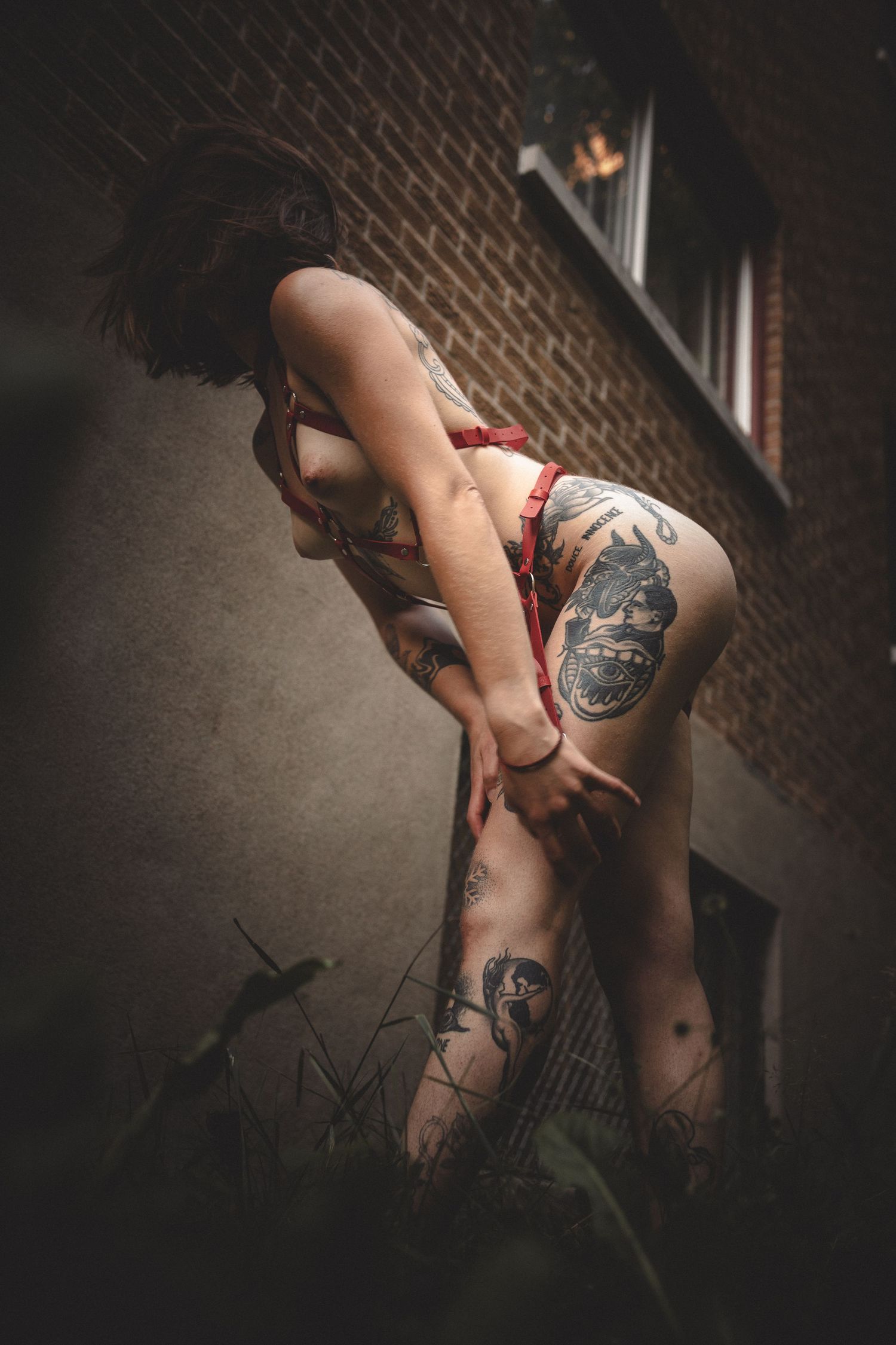 Artistic boudoir photo series showing tattooed body parts against a dark brick wall background.