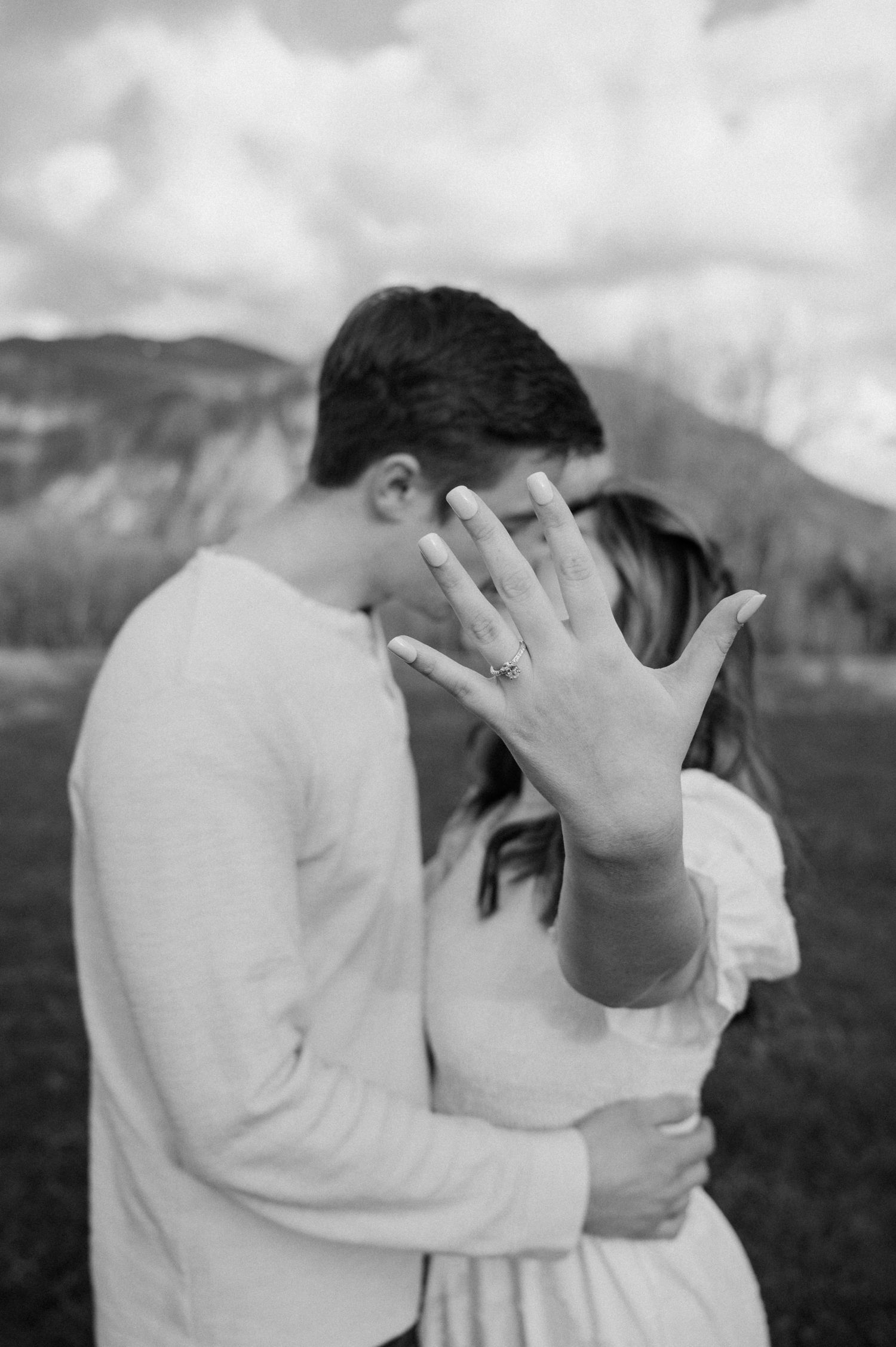 Couple in white sharing romantic moment against mountain landscape backdrop.