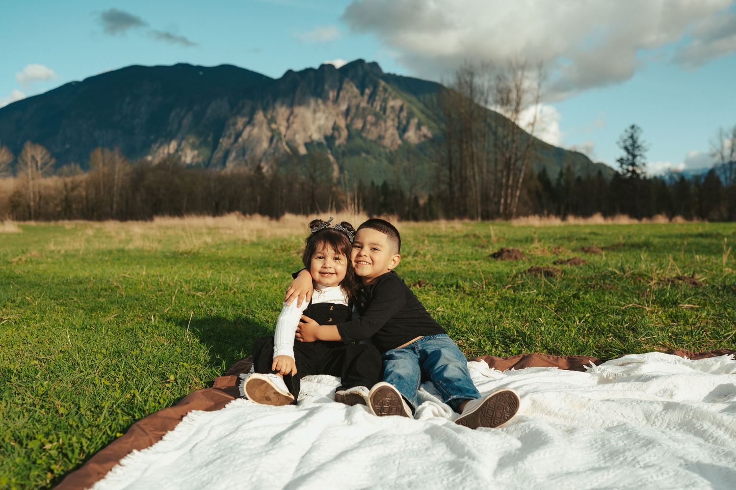 Candid family moments captured on a white blanket against mountain scenery.