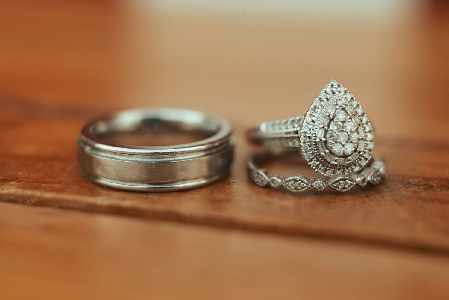 Wedding ring set featuring a vintage-style pear-shaped diamond engagement ring and classic men's wedding band on wooden surface.