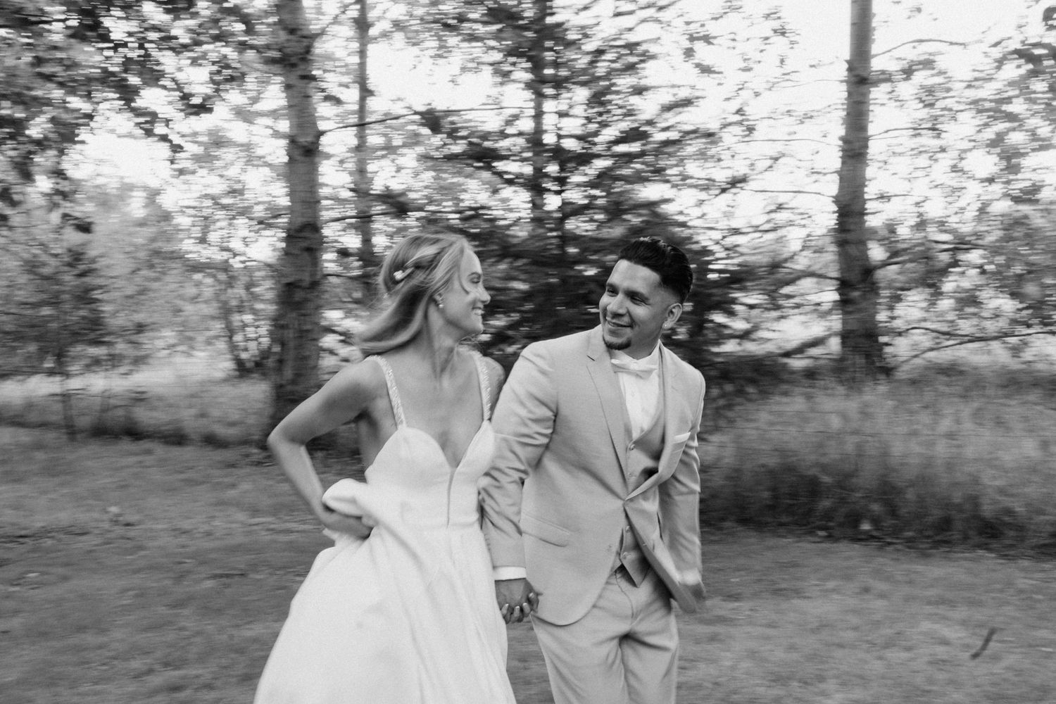 Wedding couple walking through sunlit outdoor garden setting in formal attire.
