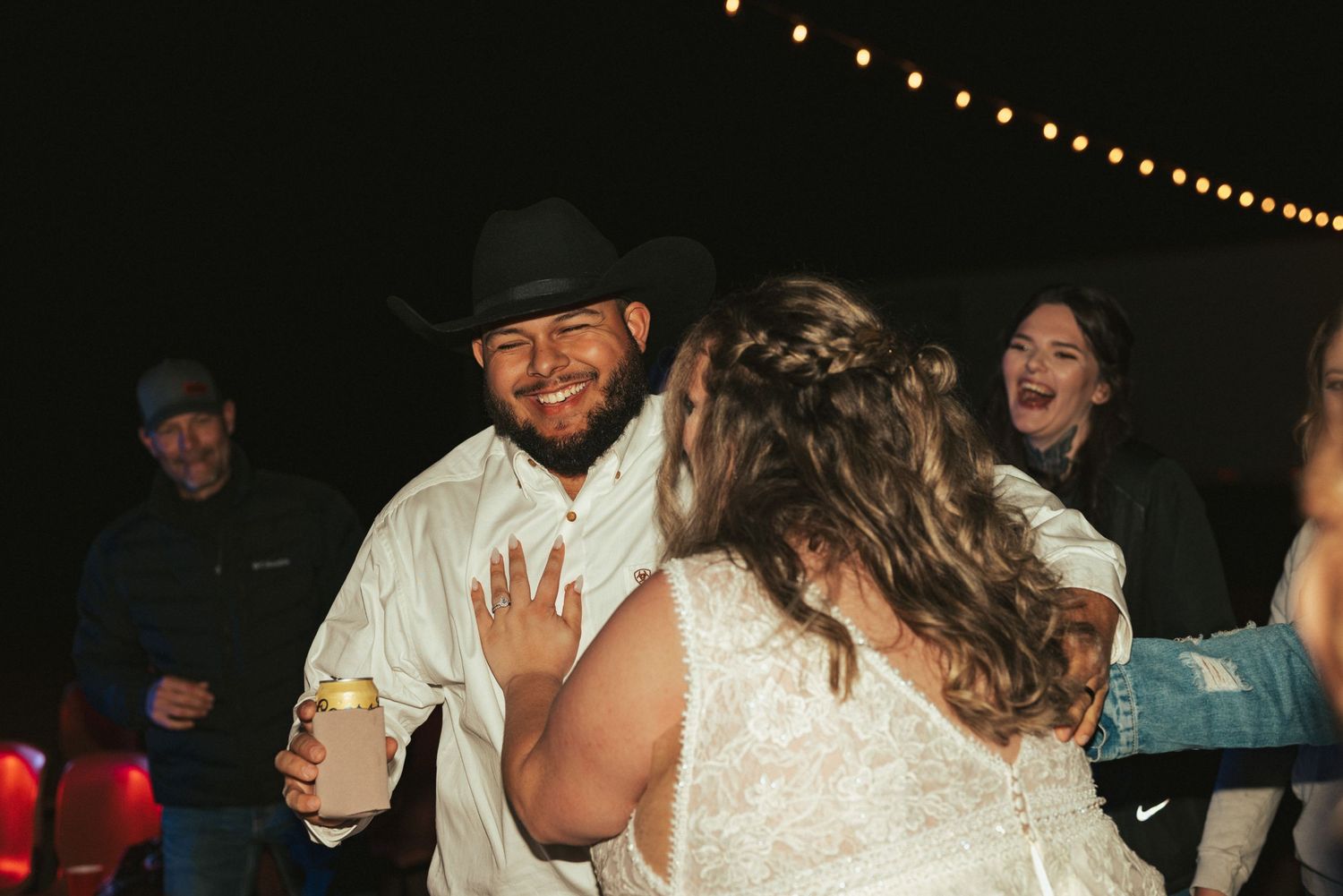 A couple dances under string lights during their evening wedding reception celebration.