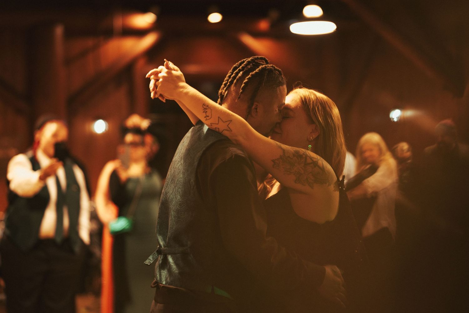 Couple dancing romantically in dim lighting at an evening event with other guests visible in the background.