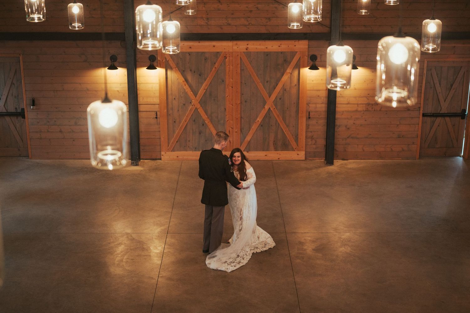A romantic wedding dance captured in a rustic barn venue illuminated by glowing glass lanterns and wall sconces.