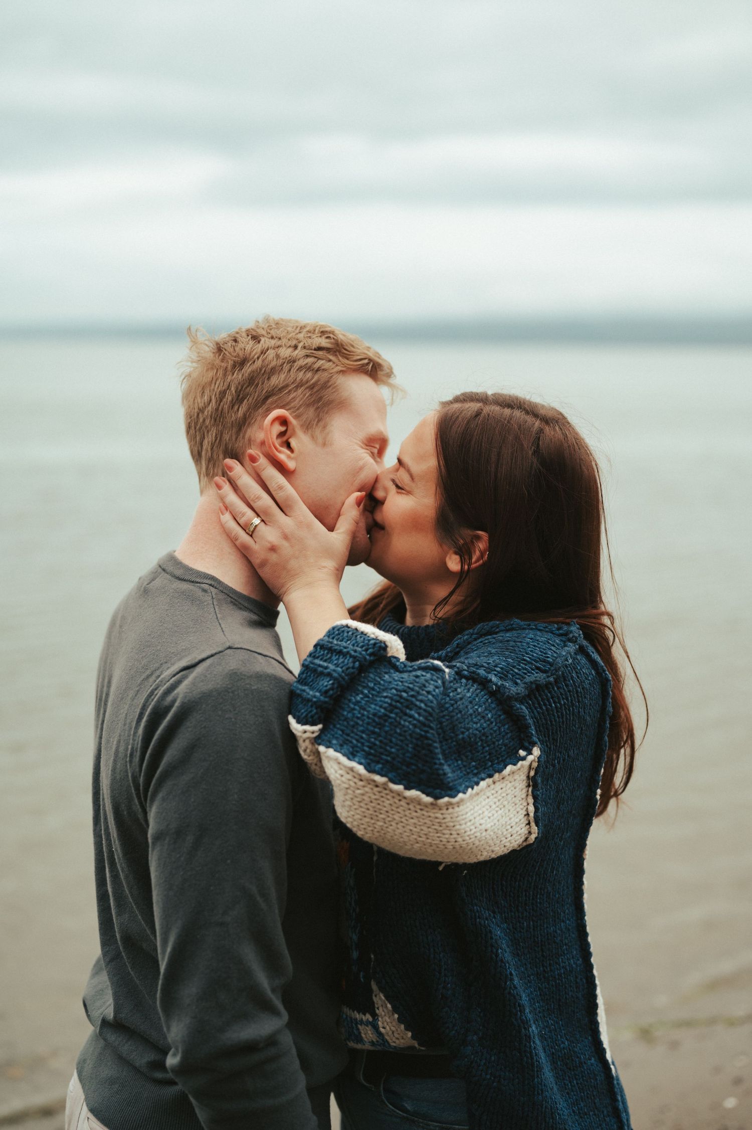 An intimate beachside moment shared between a couple with cloudy skies in the background.