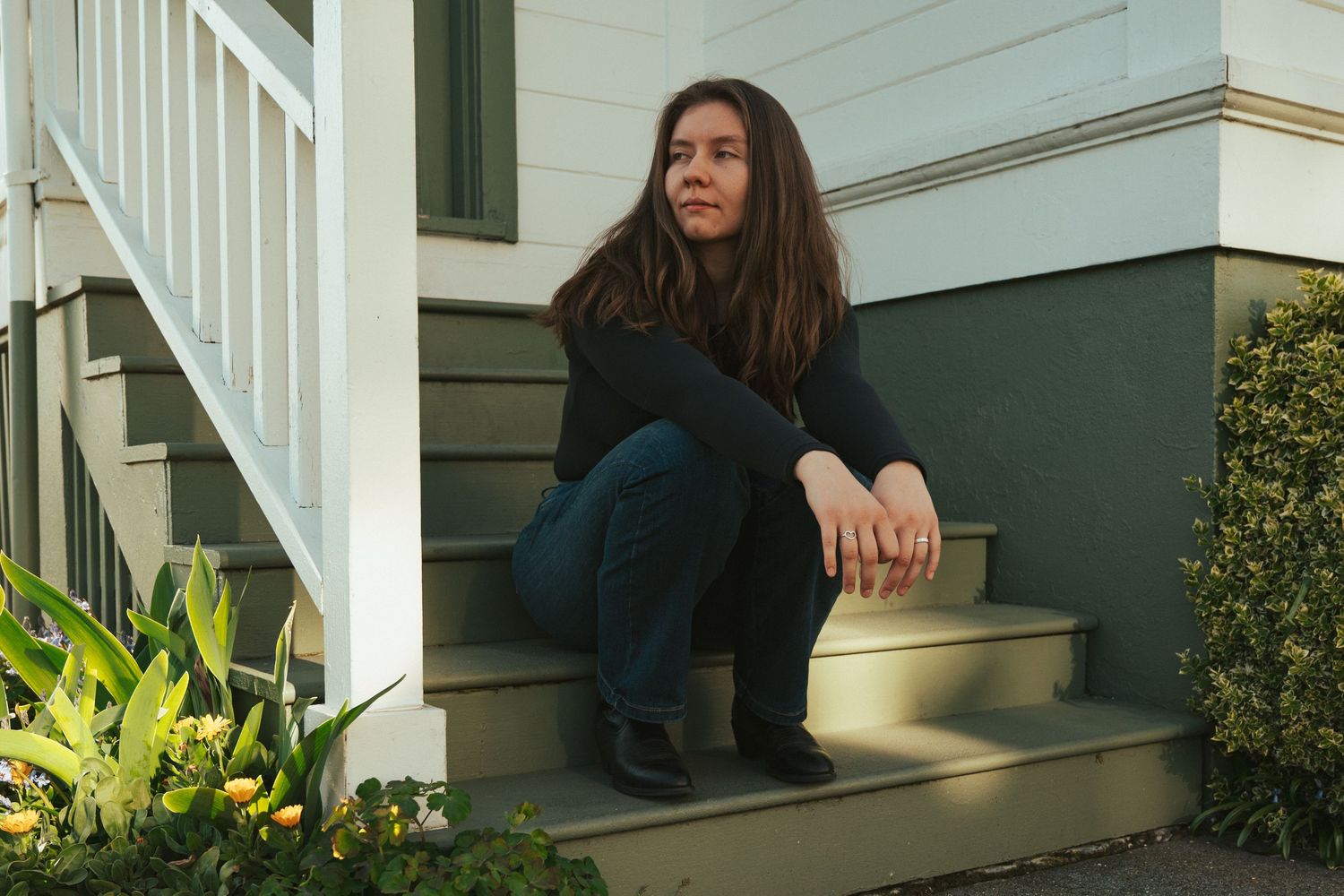 People sit casually on white porch steps during a sunny day.