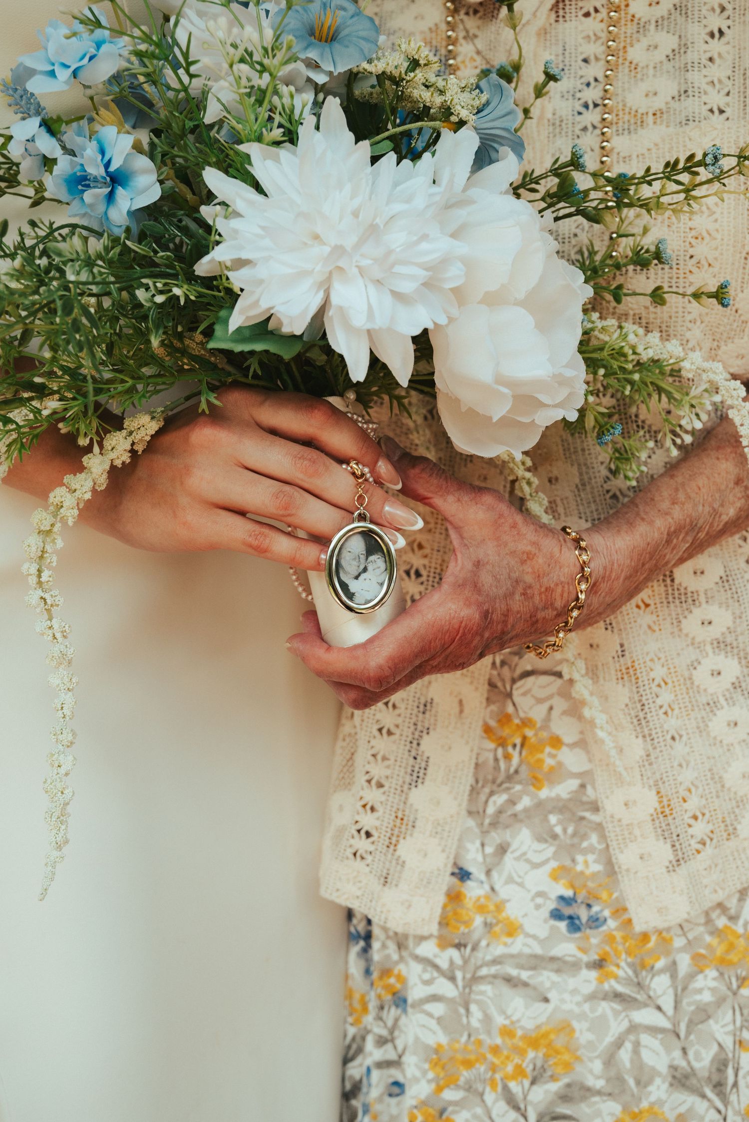 Close-up of hands holding a vintage locket with white and blue flowers in the background.