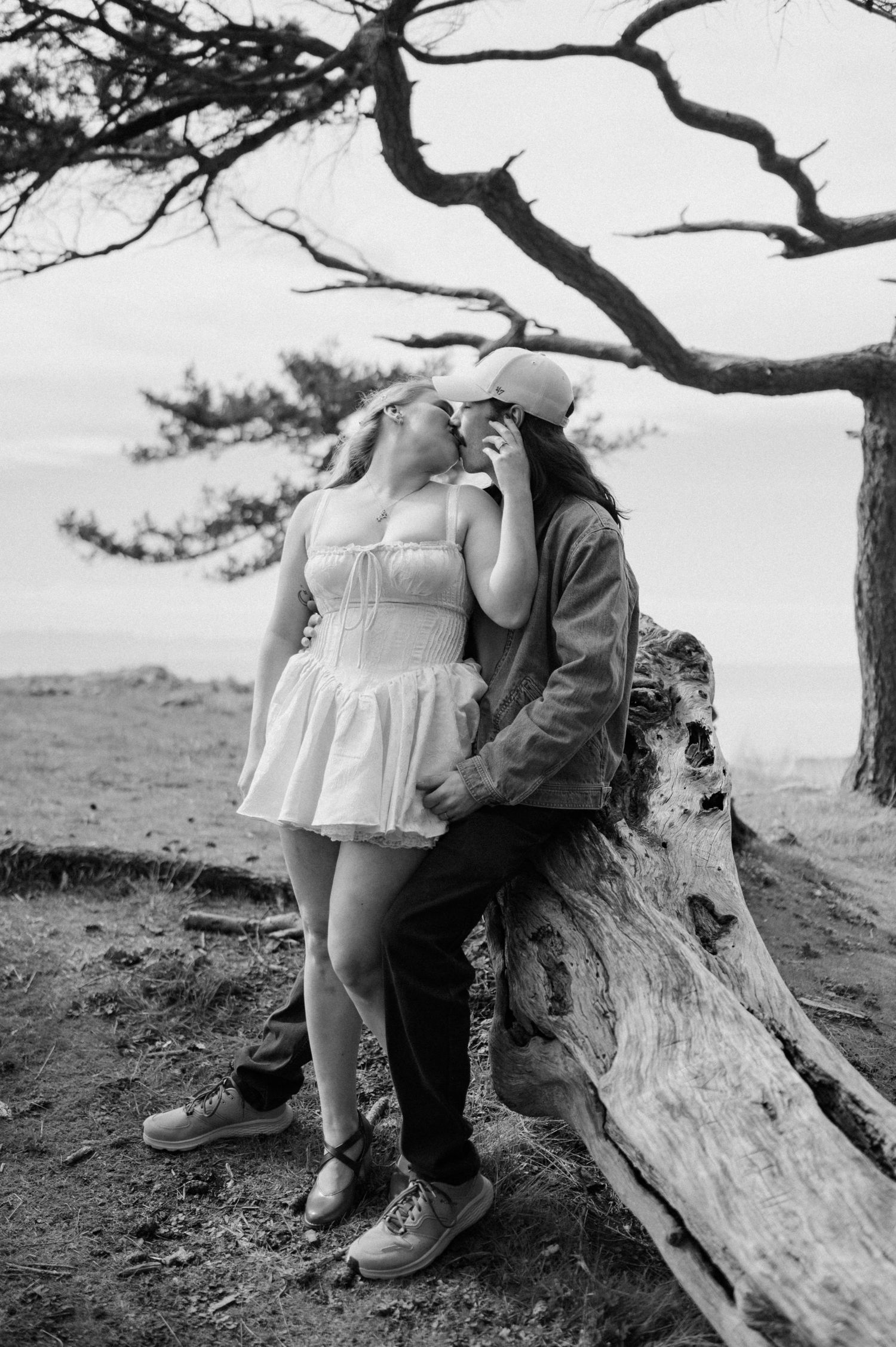 A romantic black and white photo of a couple embracing under a twisted tree branch.