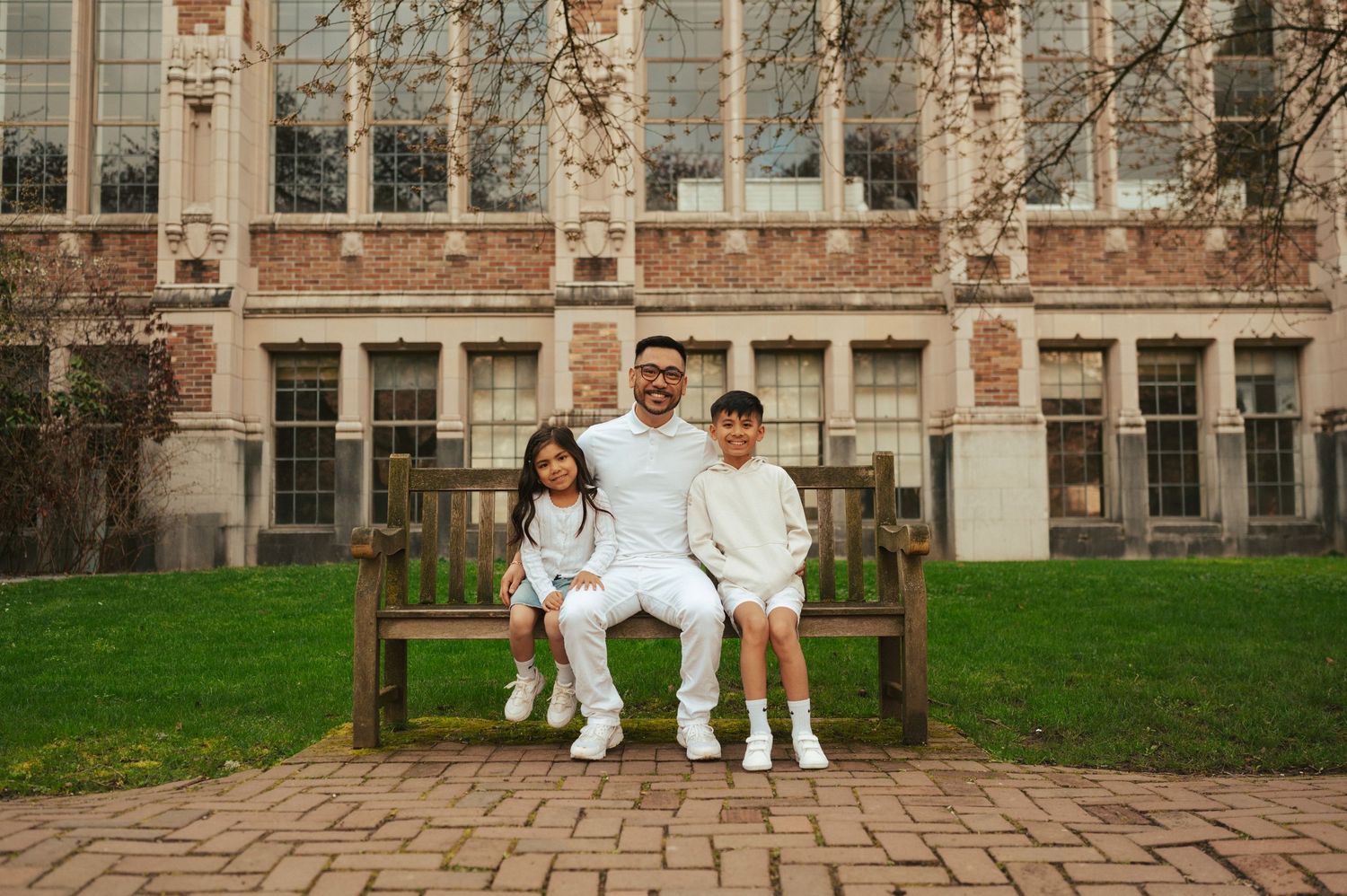 A group sits together on a wooden bench in front of a brick university building.