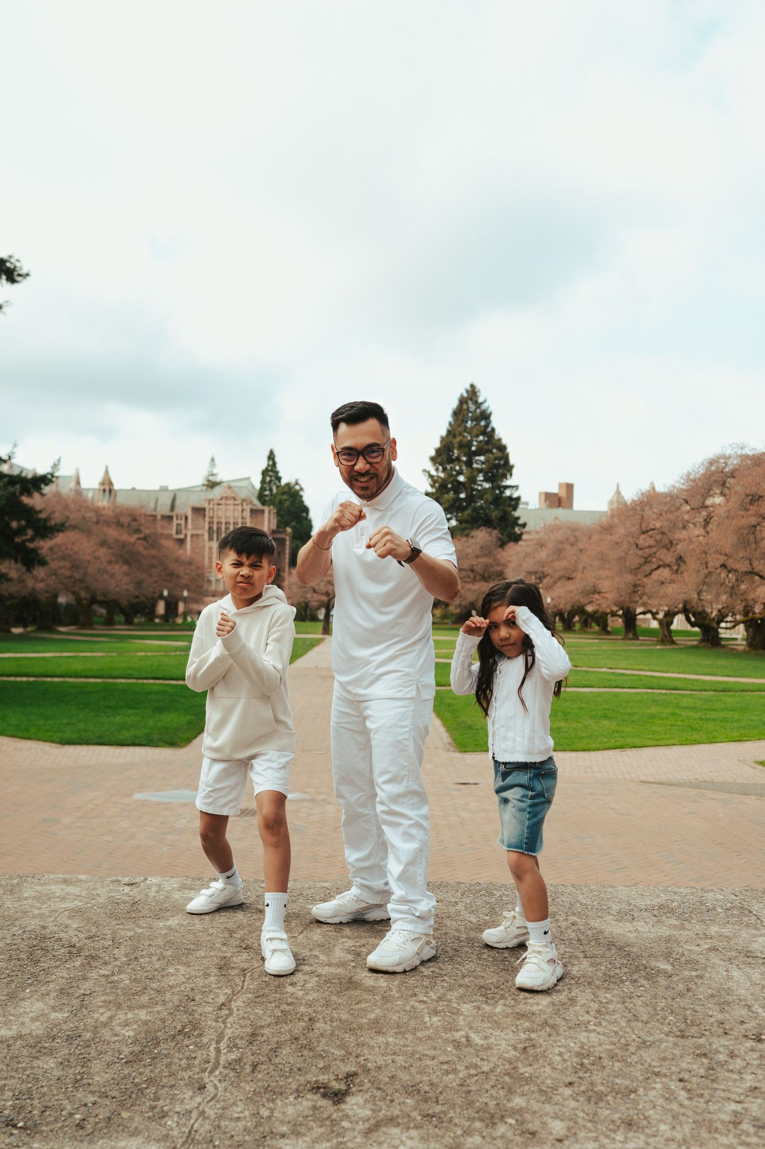 Three people in coordinated white outfits strike playful poses outdoors.