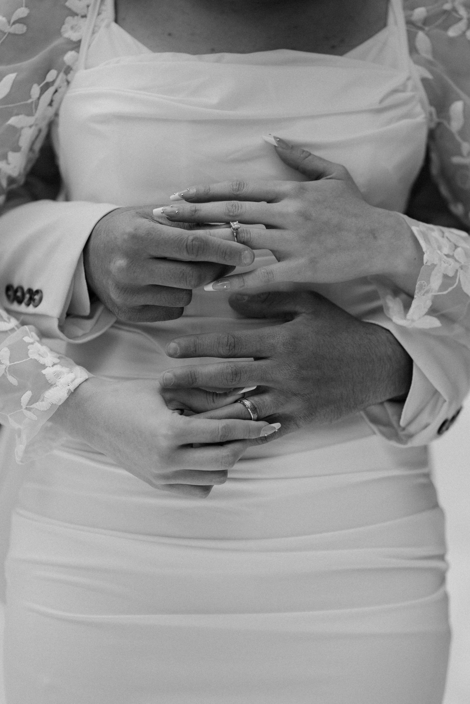 Wedding detail shot showing hands with rings resting on white dress fabric.