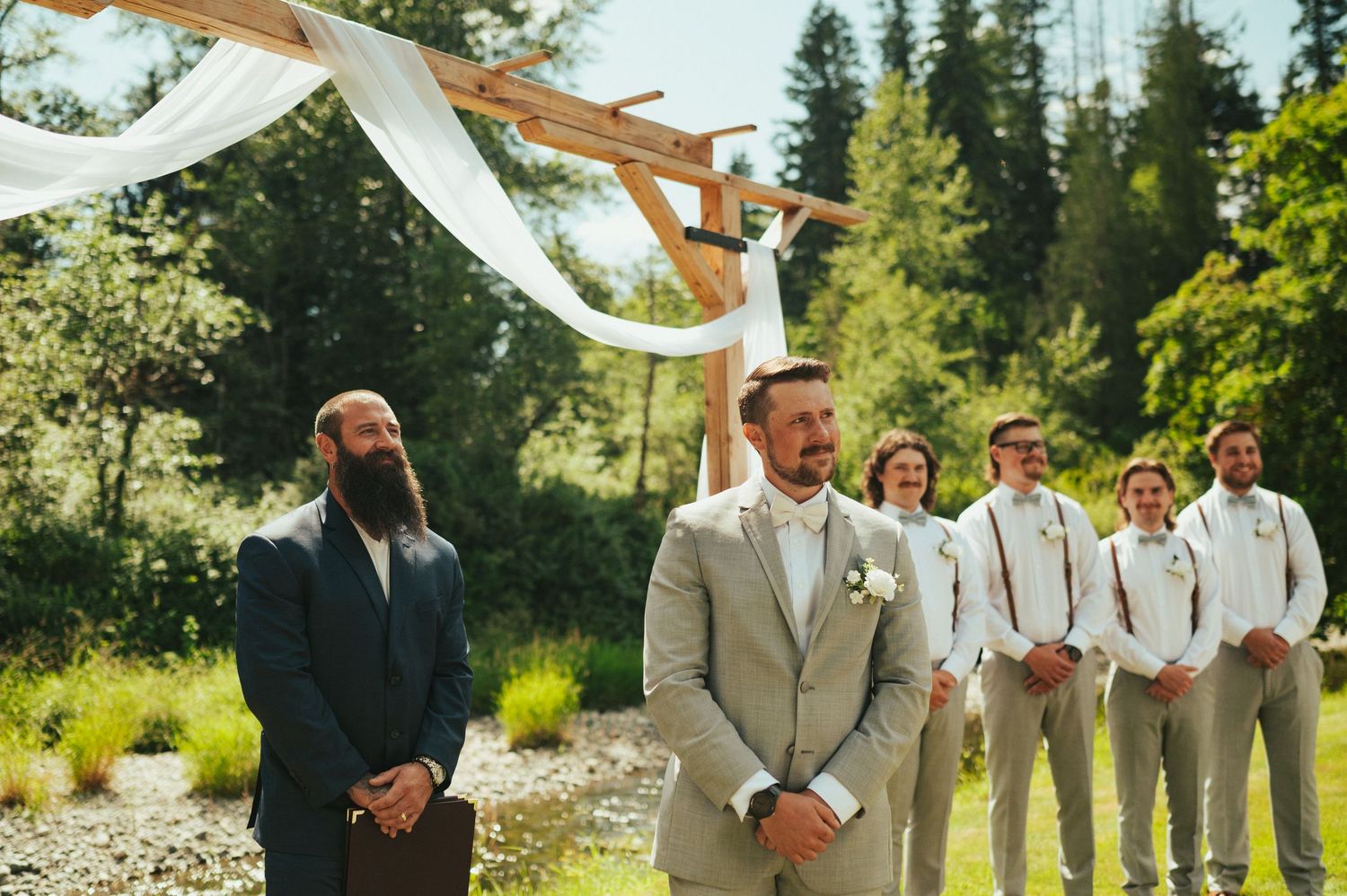 Wedding ceremony setup with flowing white fabric and groomsmen standing outdoors.
