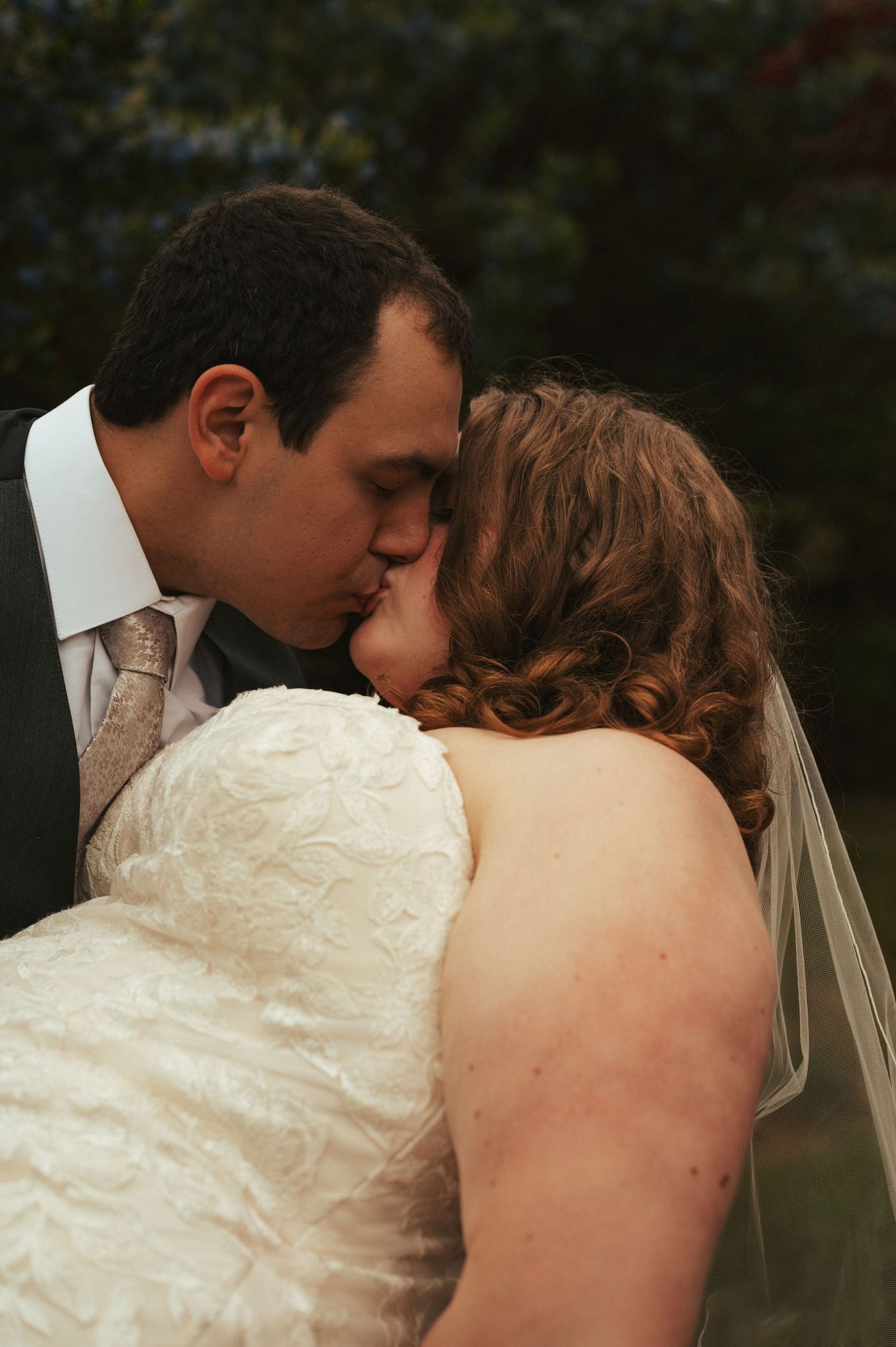 A romantic kiss between newlyweds, with the bride wearing a white lace dress and veil.
