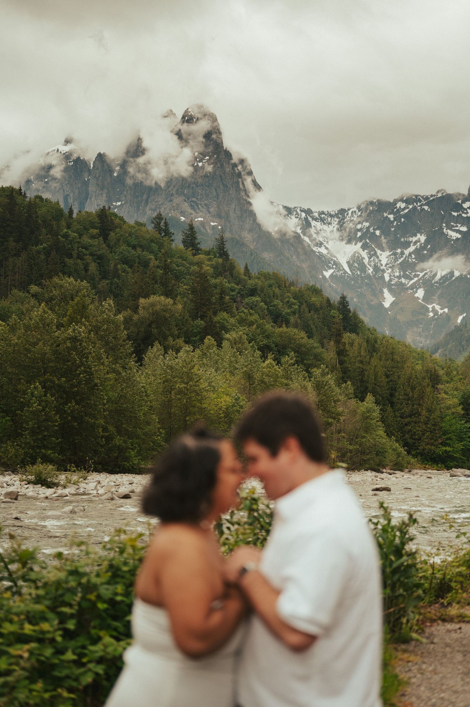 A romantic moment captured against a backdrop of misty mountain peaks with snow-capped summits.