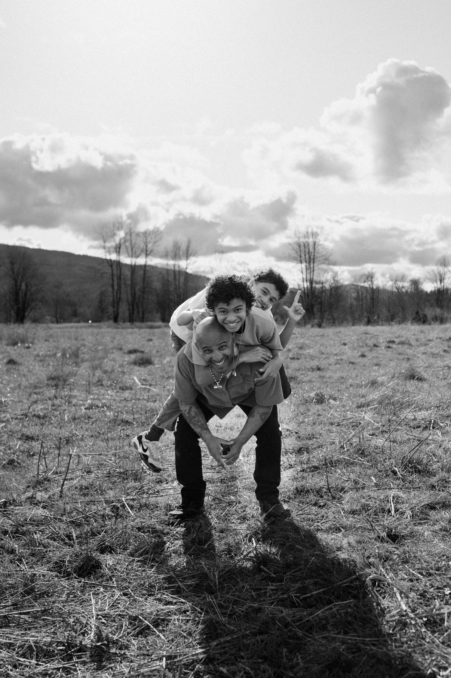 Black and white photograph of playful interactions in an open field with mountain views.