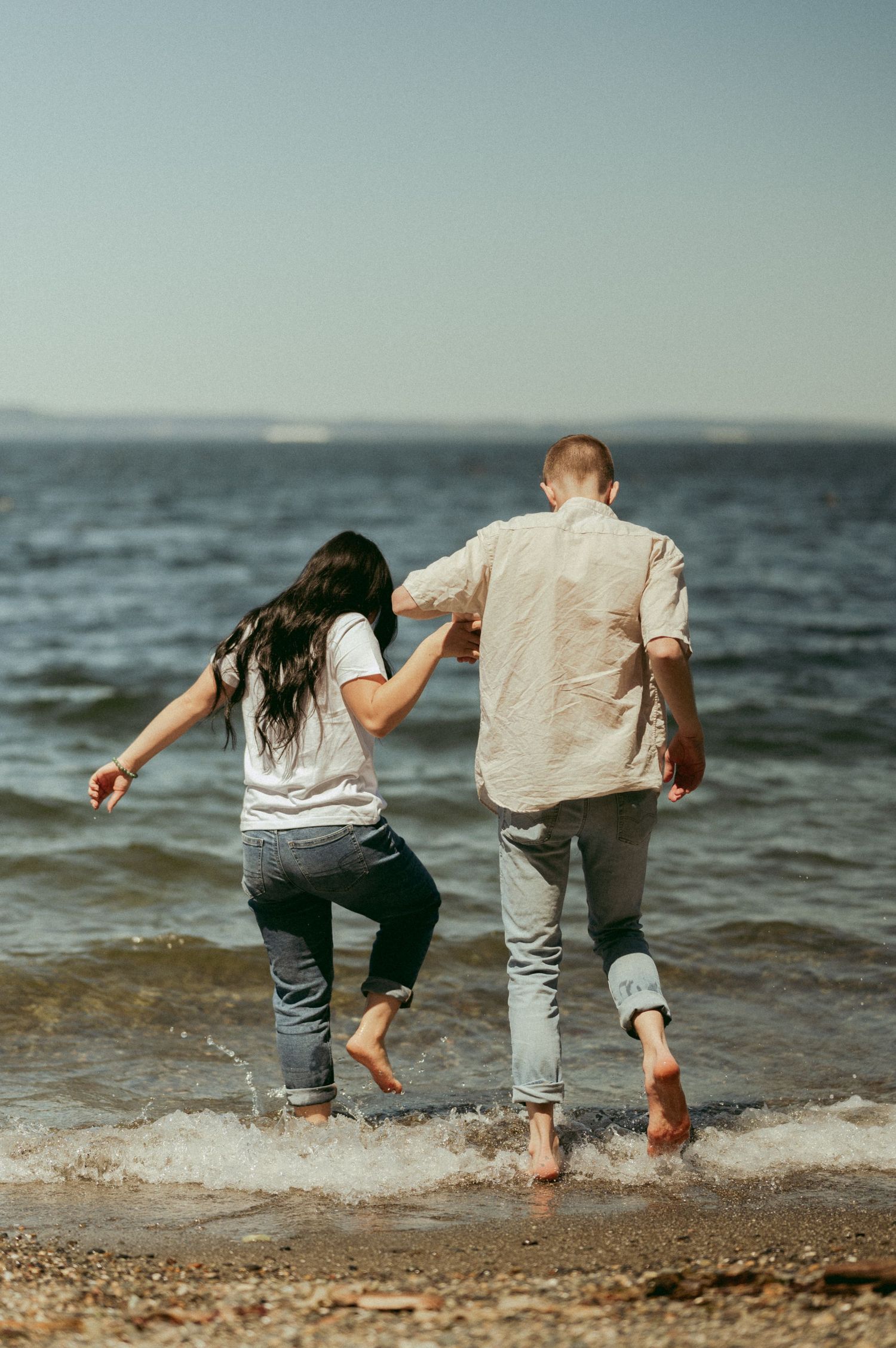 A couple splashes in the ocean waves together at the beach.