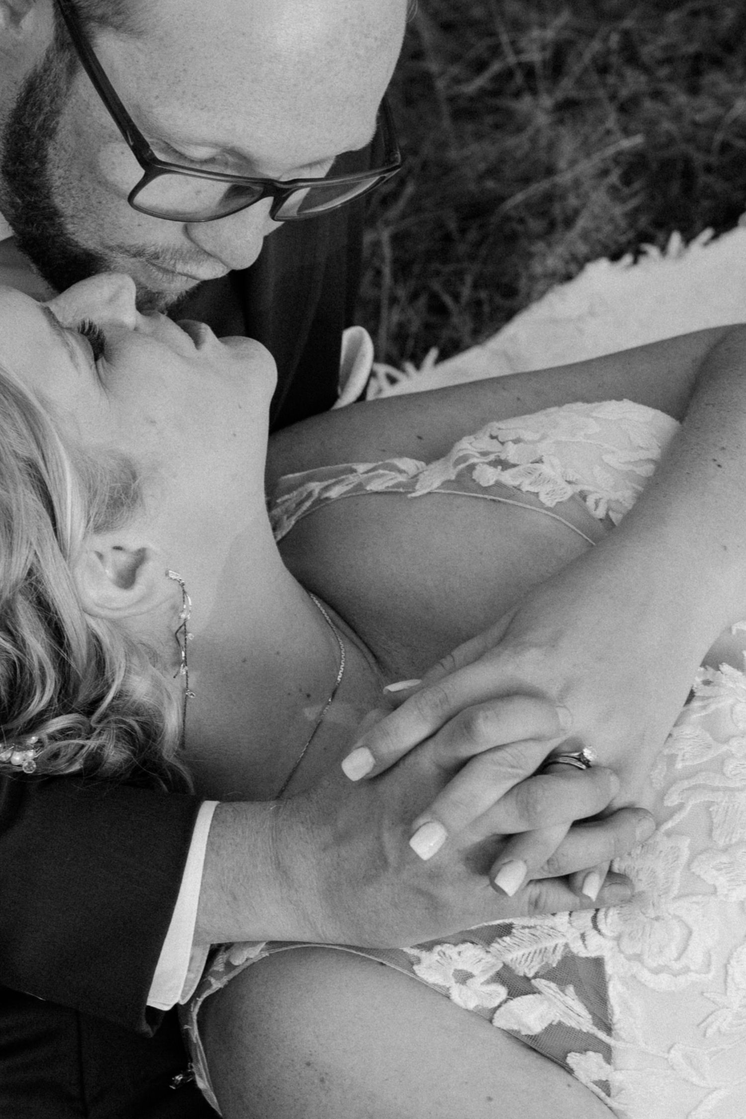 Black and white close-up details of lace wedding dress and hands.
