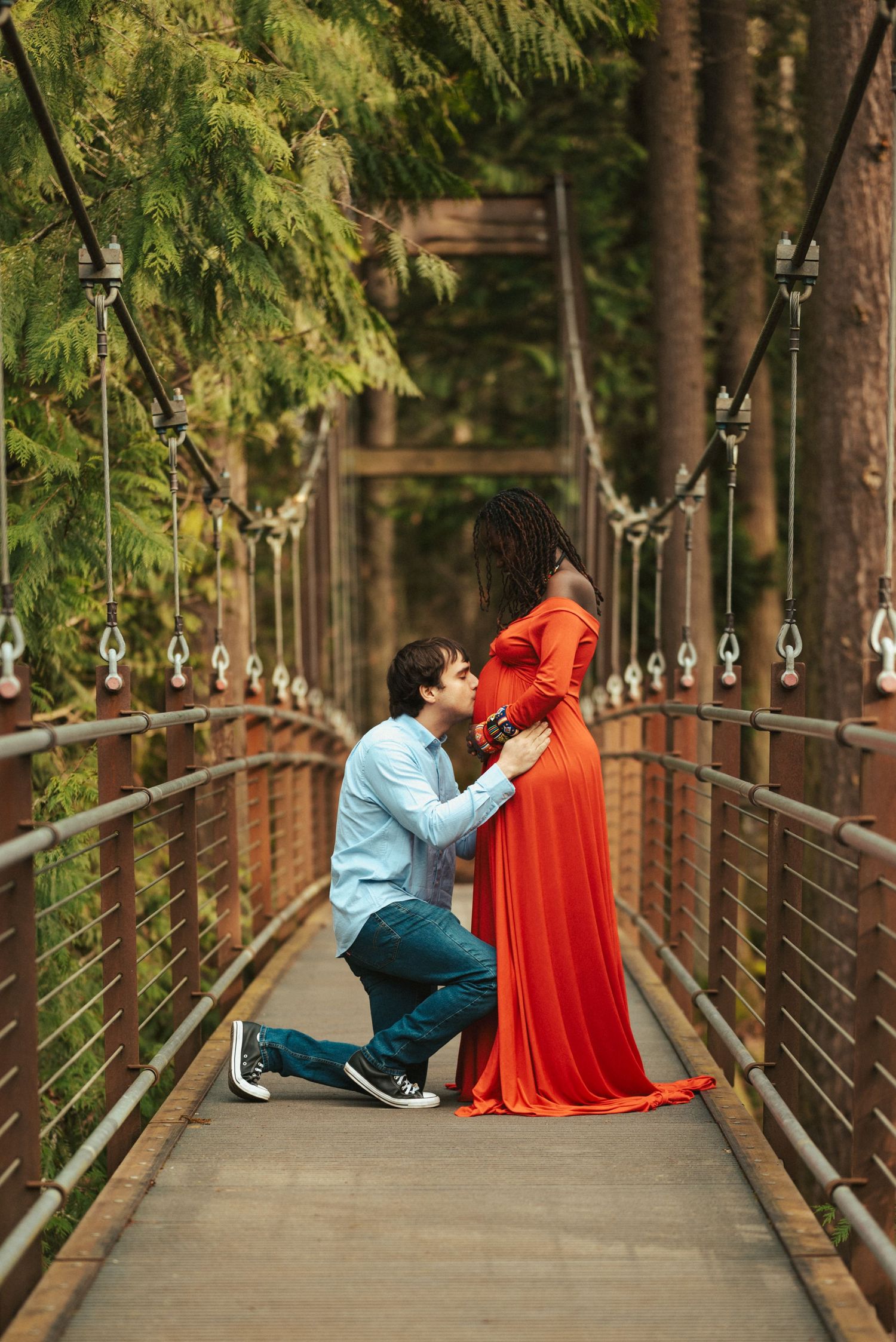 A romantic proposal moment captured on a wooden bridge surrounded by tall evergreen trees.