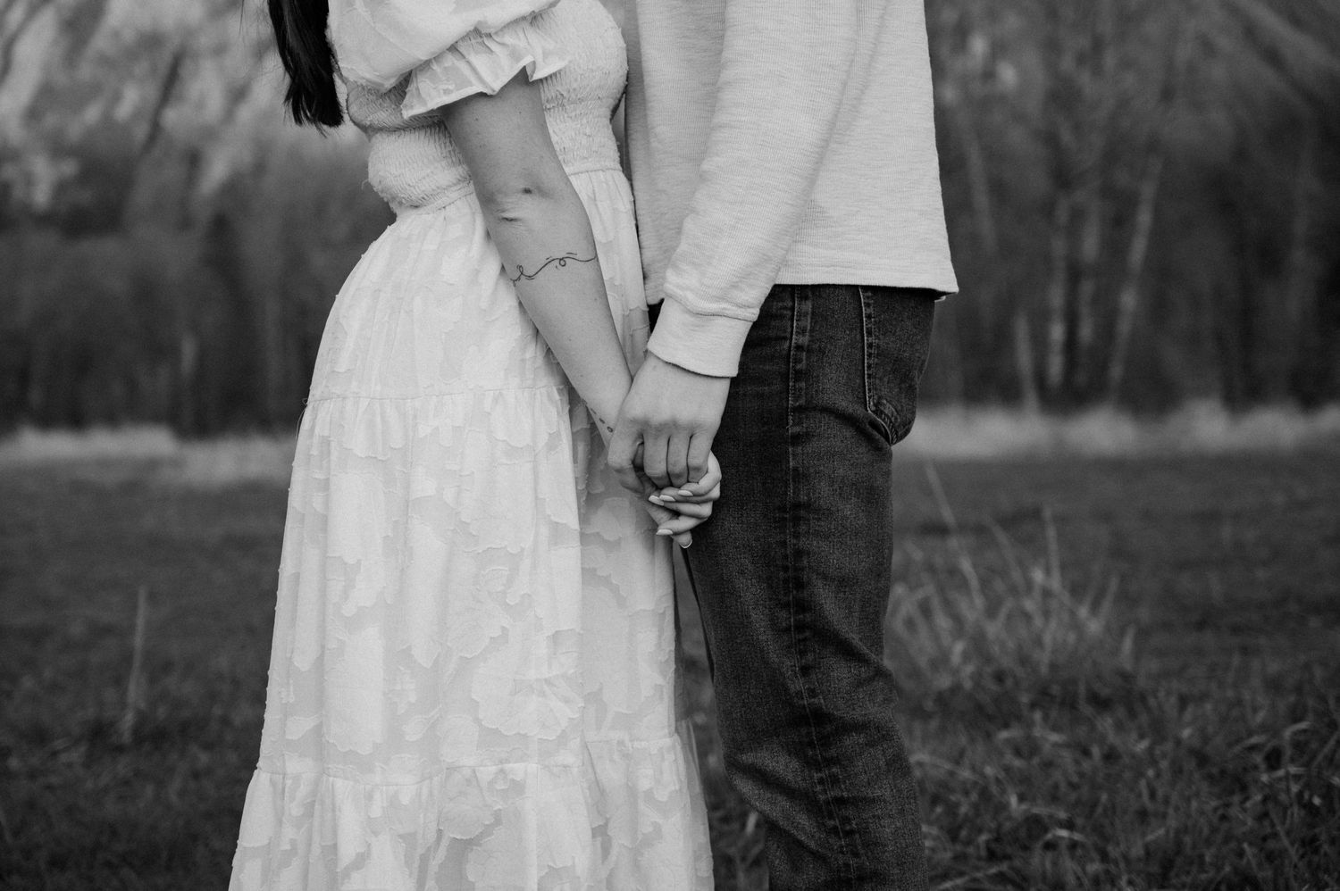 A close-up black and white shot of a couple holding hands in formal attire.