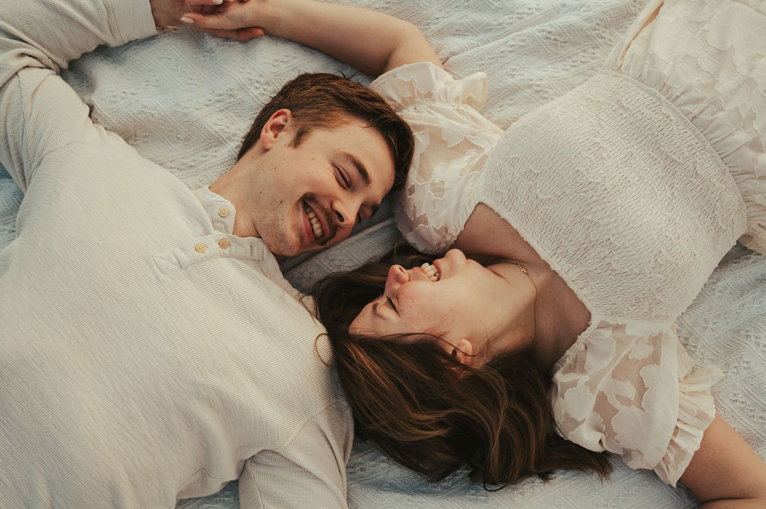 Couple laying together intimately on white blanket during photo session.