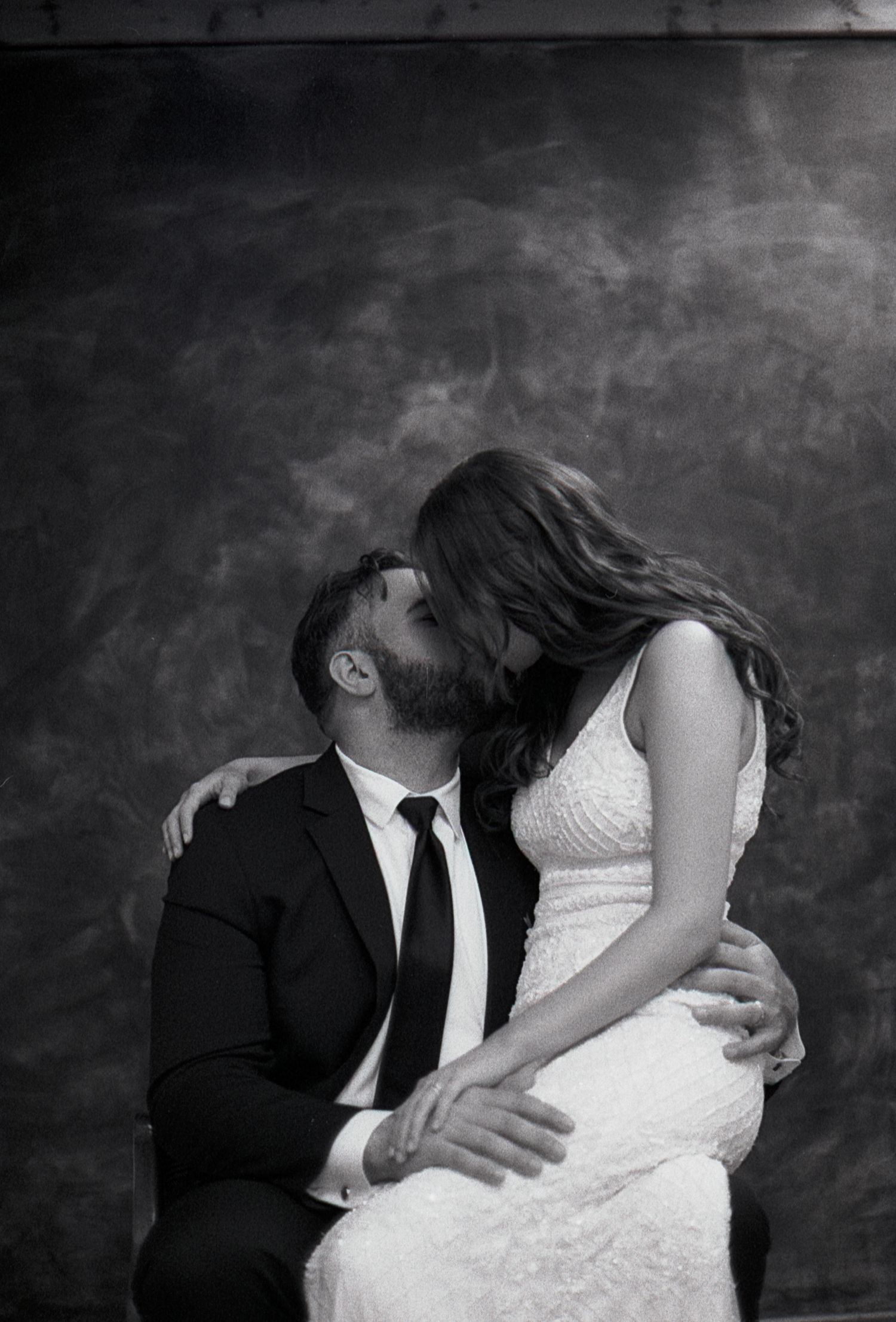 An intimate black and white portrait of a couple embracing in formal wedding attire.
