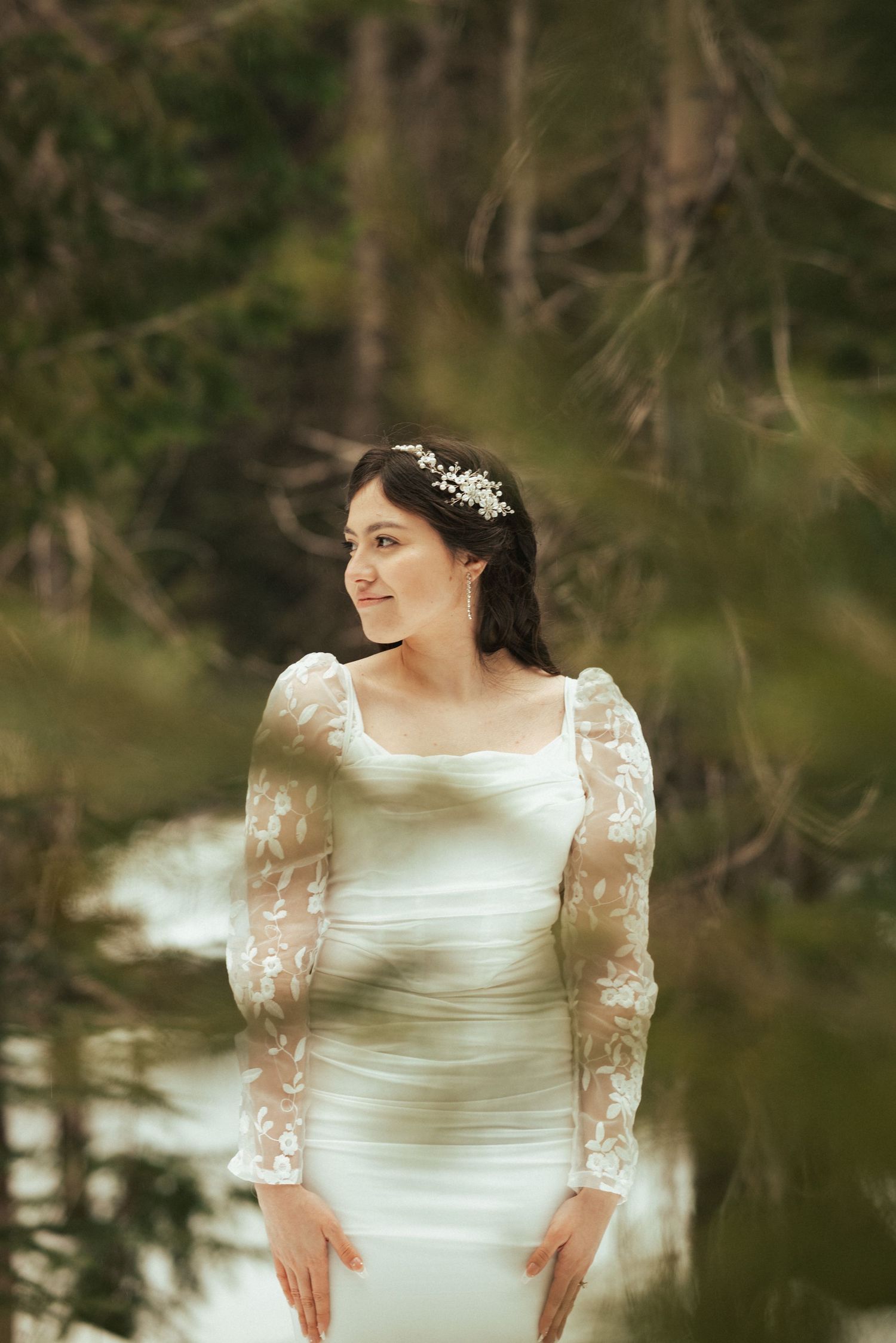 White wedding dress with delicate lace sleeves captured in natural forest setting.