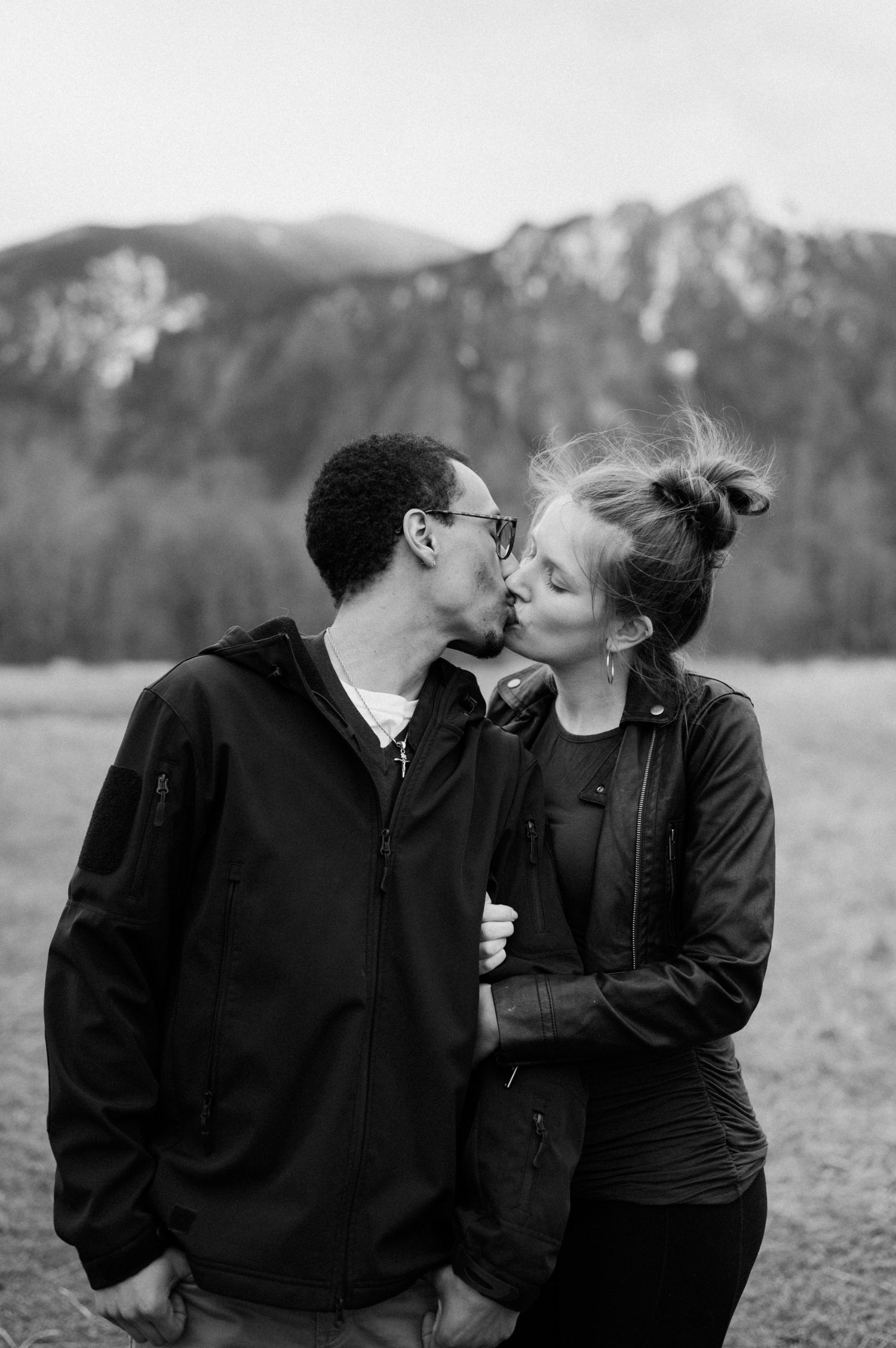 An intimate black and white photo series showing affectionate moments in front of mountain scenery.
