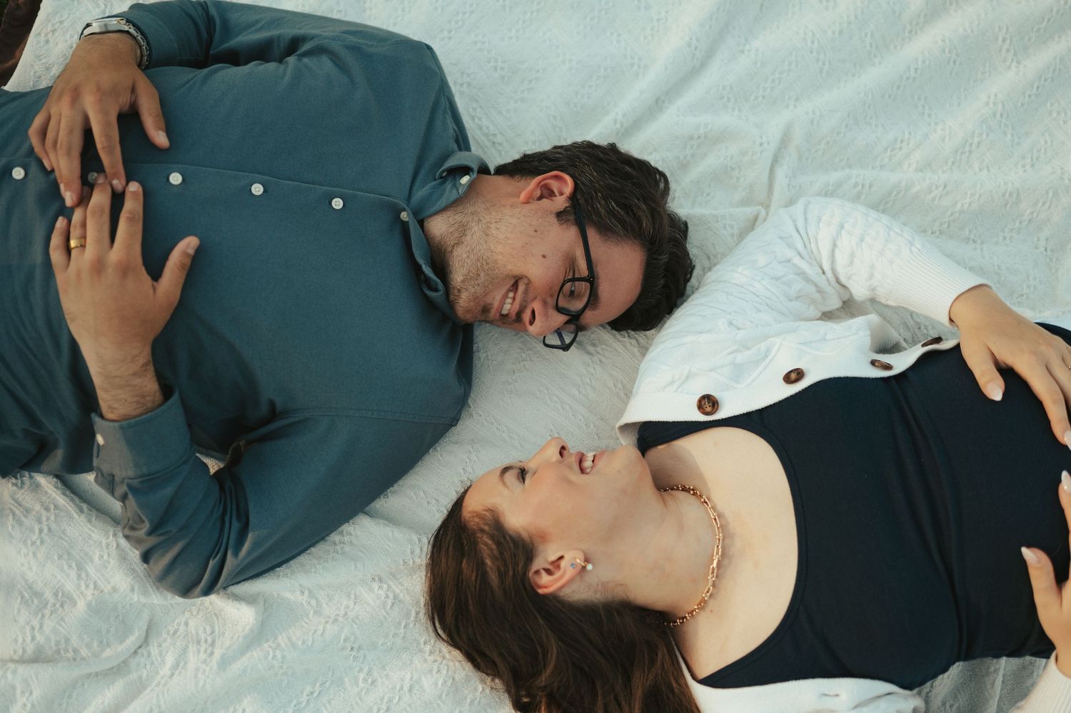 A couple laughing while lying on a white blanket outdoors.