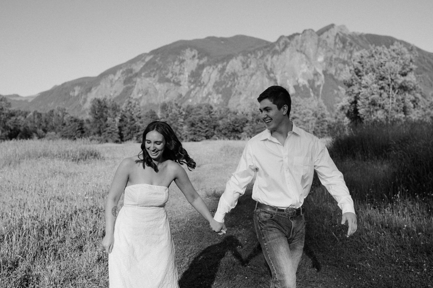 A black and white photo of a couple running through a mountain meadow.