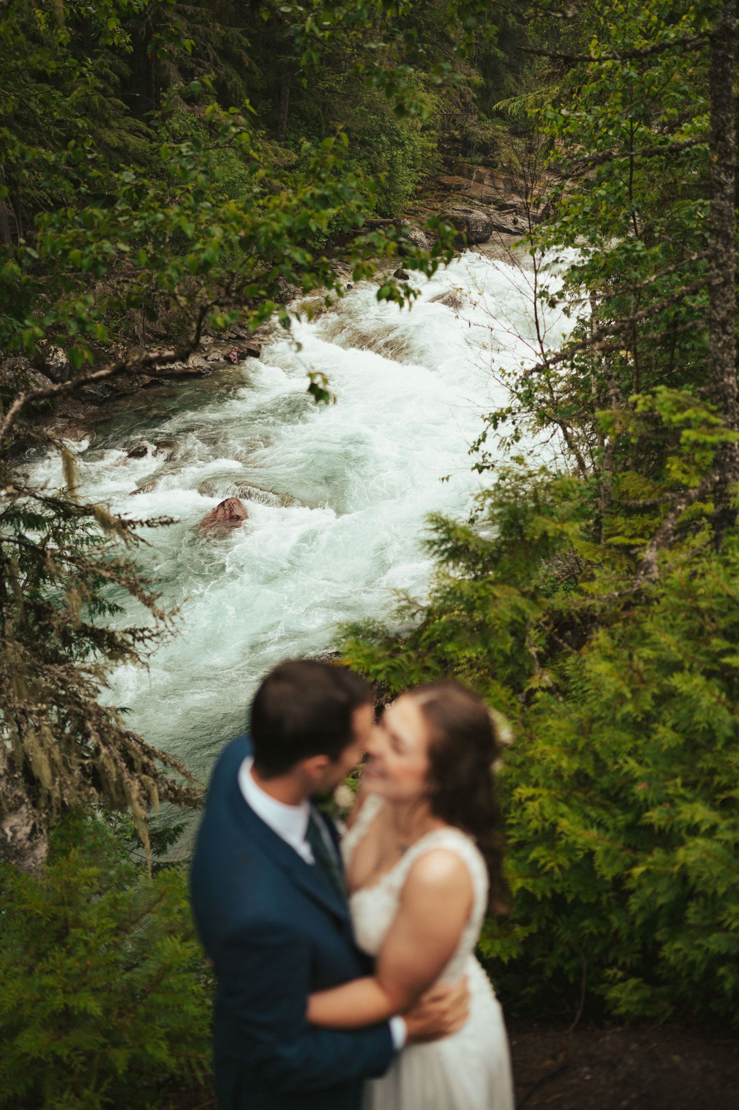A romantic moment captured above rushing white water rapids in a forest setting.
