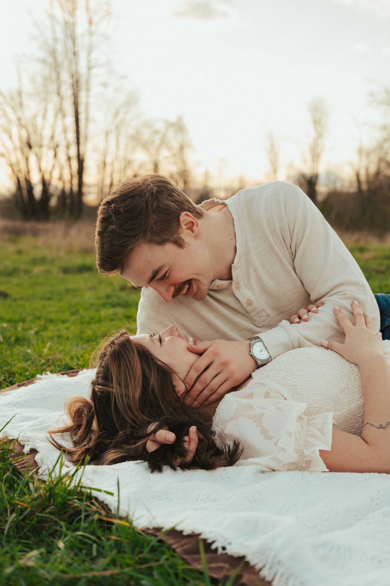 Romantic couple sharing tender moments on white blanket in spring field.