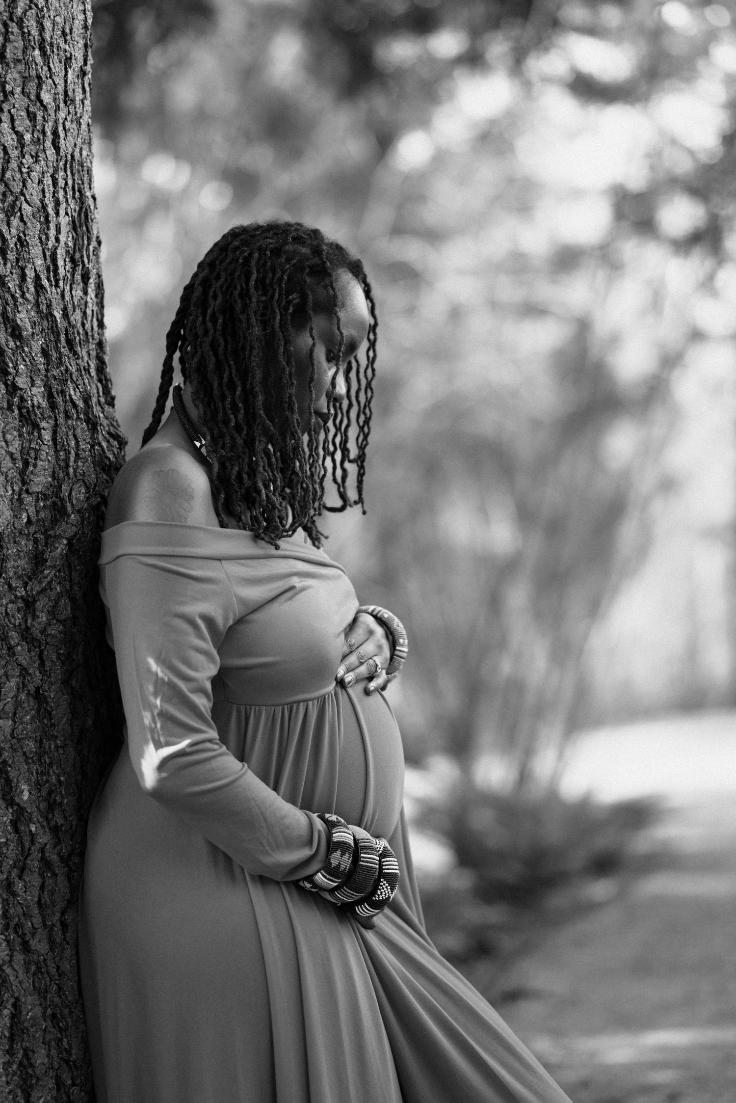A black and white portrait showing an elegant maternity pose against a tree.