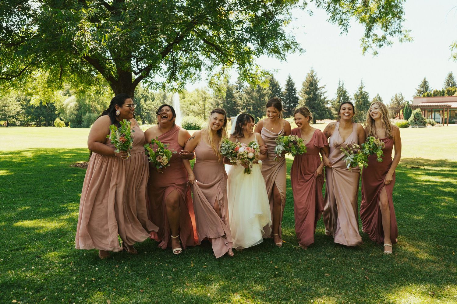 Bridal party in blush pink dresses poses together on a sunny lawn.
