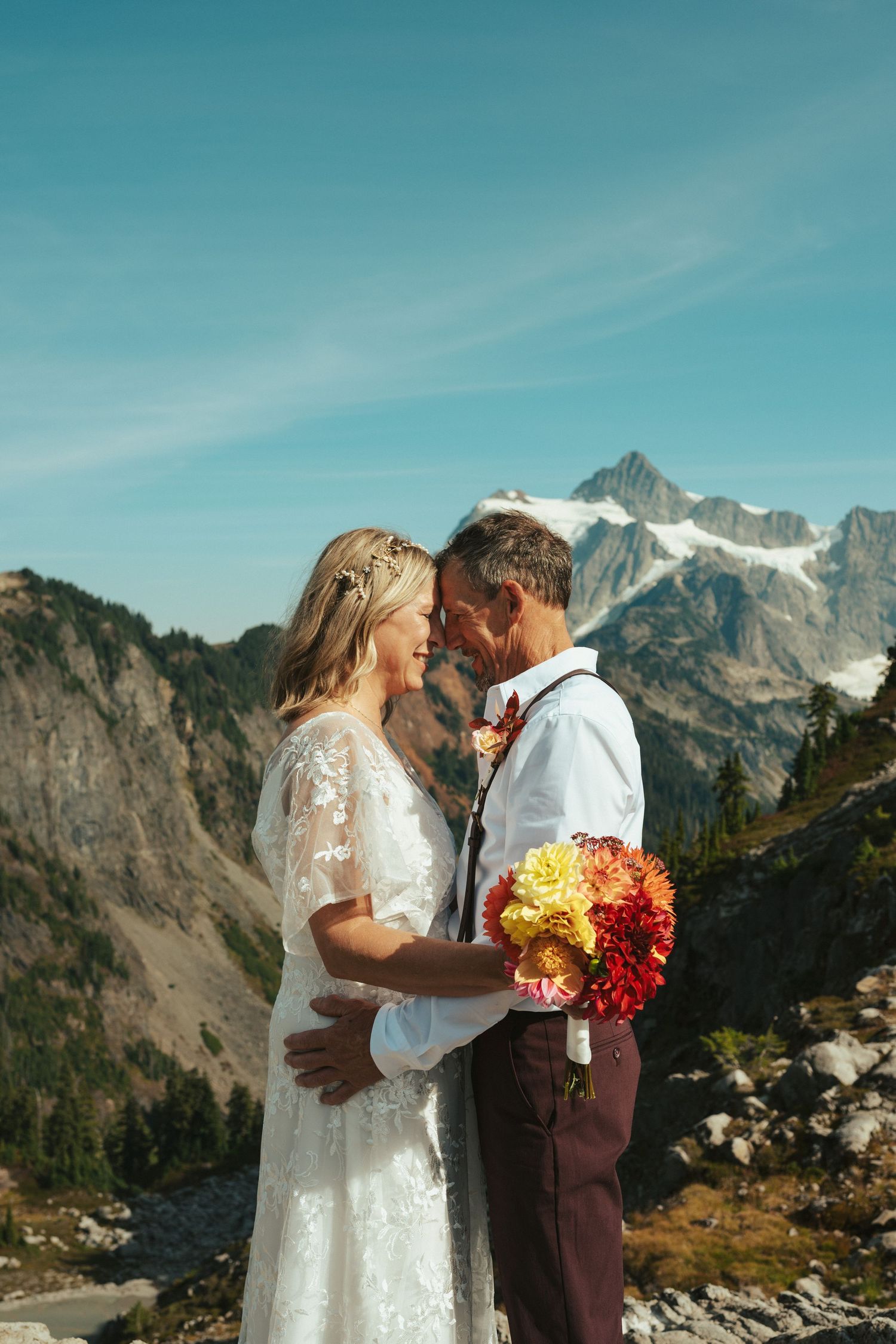 A couple shares a romantic moment in front of majestic mountain peaks during their outdoor wedding ceremony.