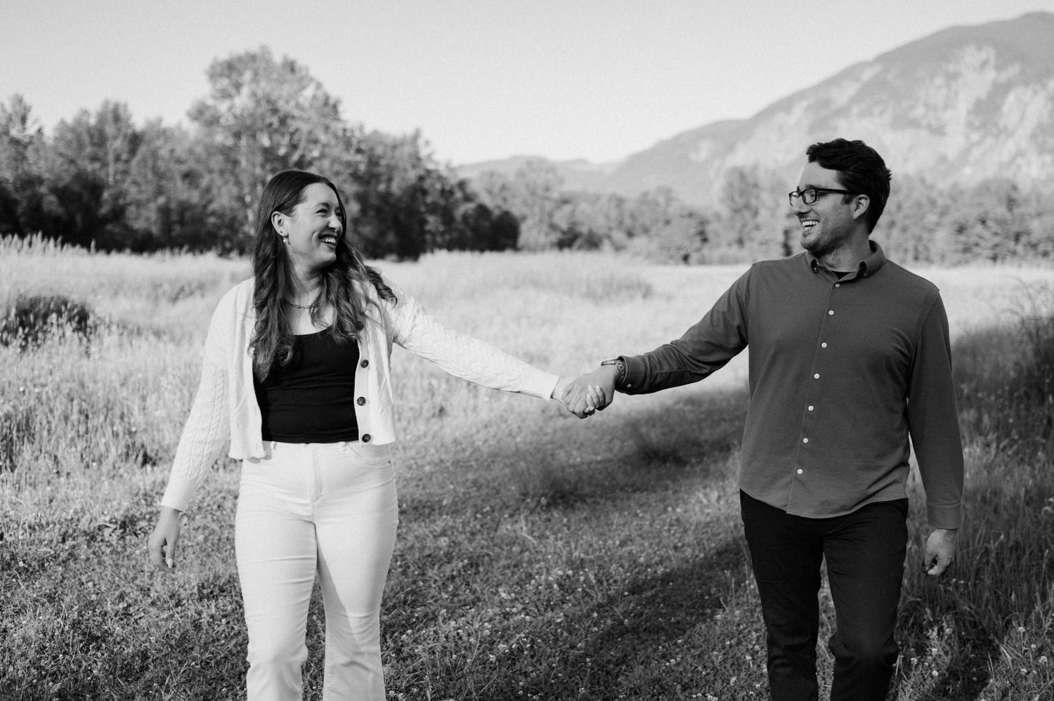 A black and white photo of a couple sharing a lighthearted moment in a mountain field.