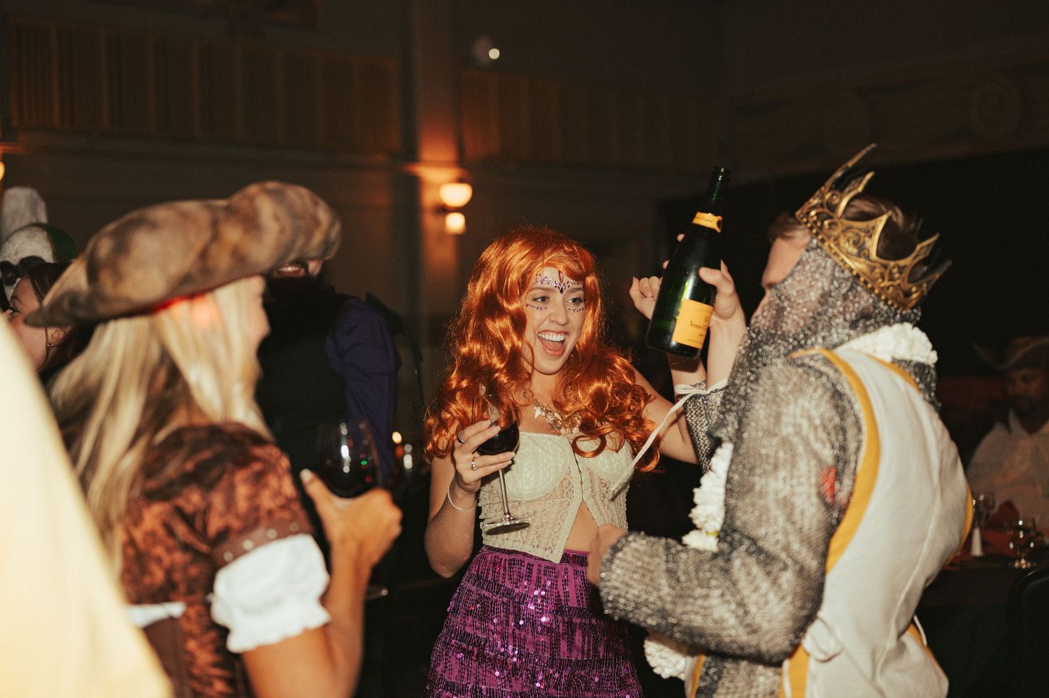Costumed partygoers dance and celebrate at a nighttime indoor masquerade or Halloween event.