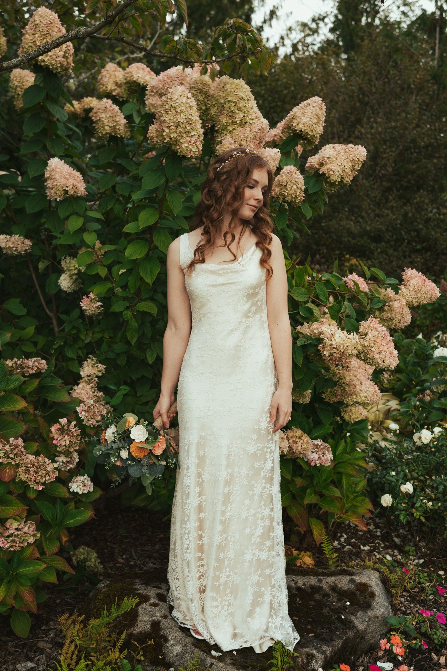 Lace wedding dress against a backdrop of blooming hydrangea bushes in a garden setting.